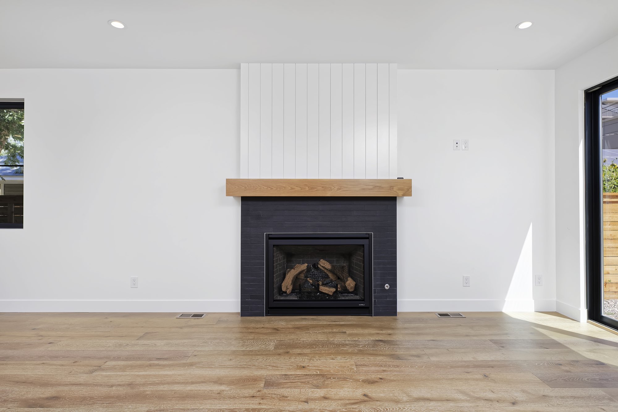 Living room with a gas fireplace in a dark tile surround, a wood mantel, white vertical paneling above and wide-plank light wood floors