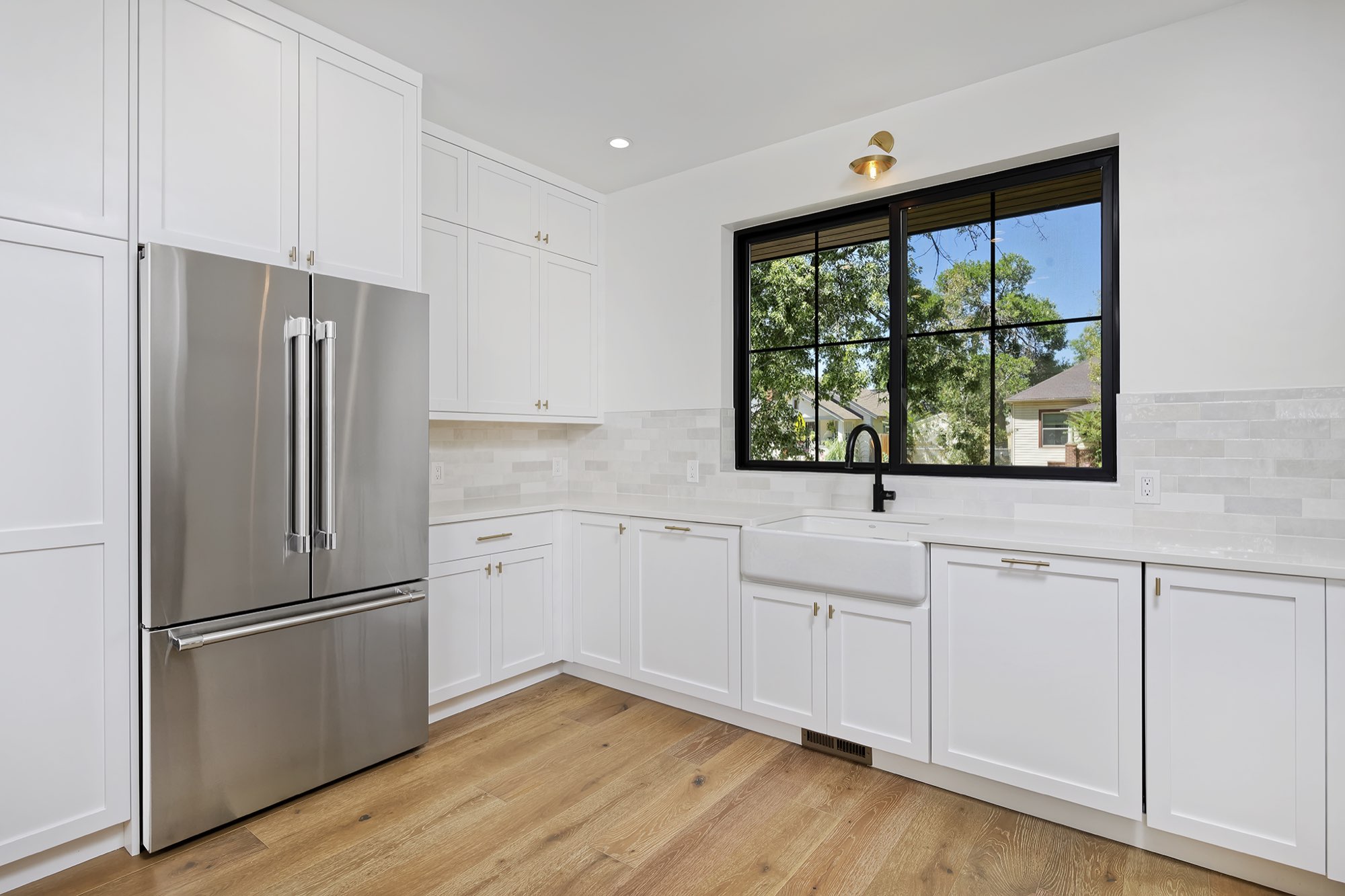 White kitchen with a stainless refrigerator, farmhouse sink and a large black-framed window