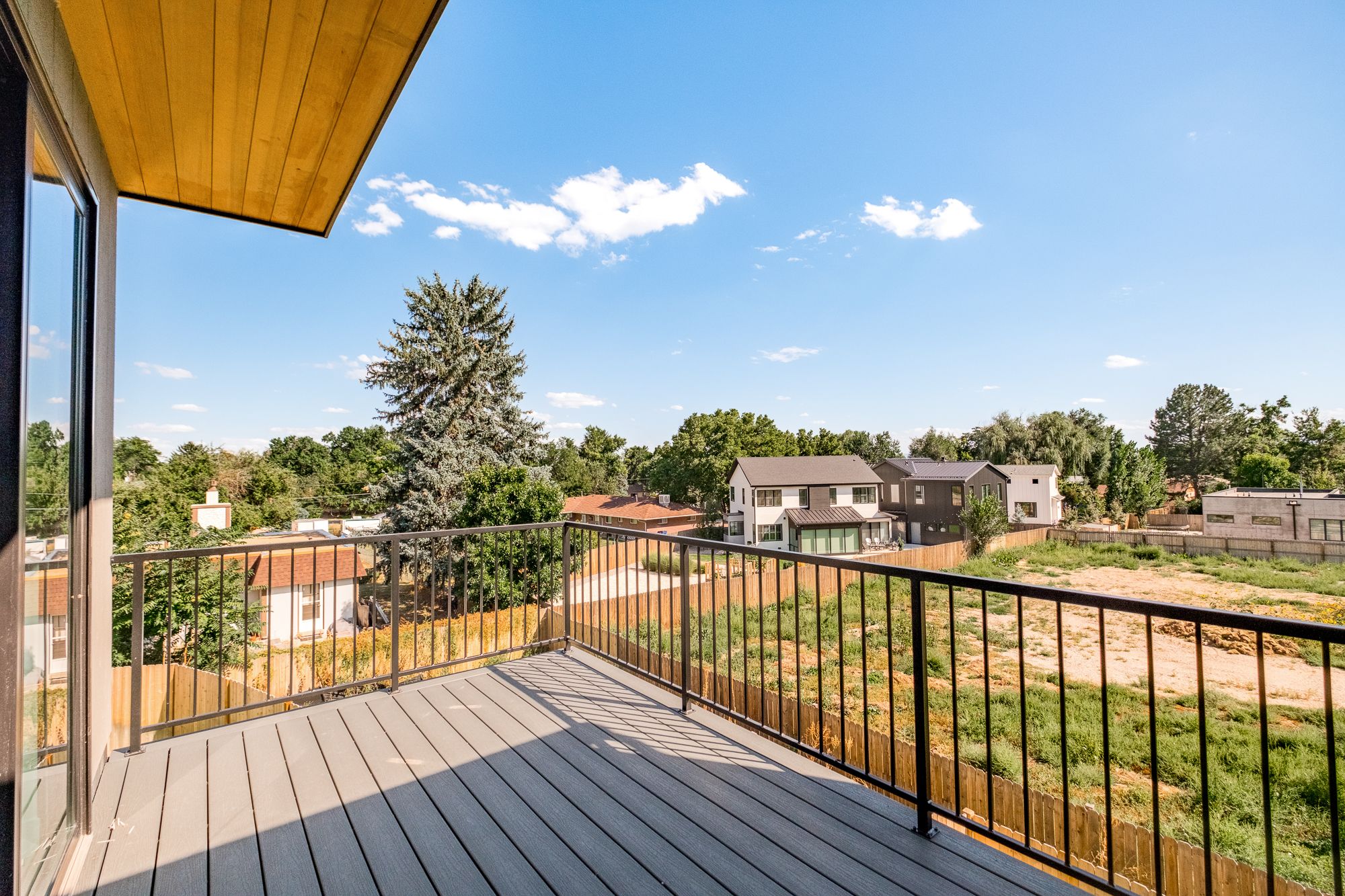 Upper balcony with a black metal railing under a wood soffit