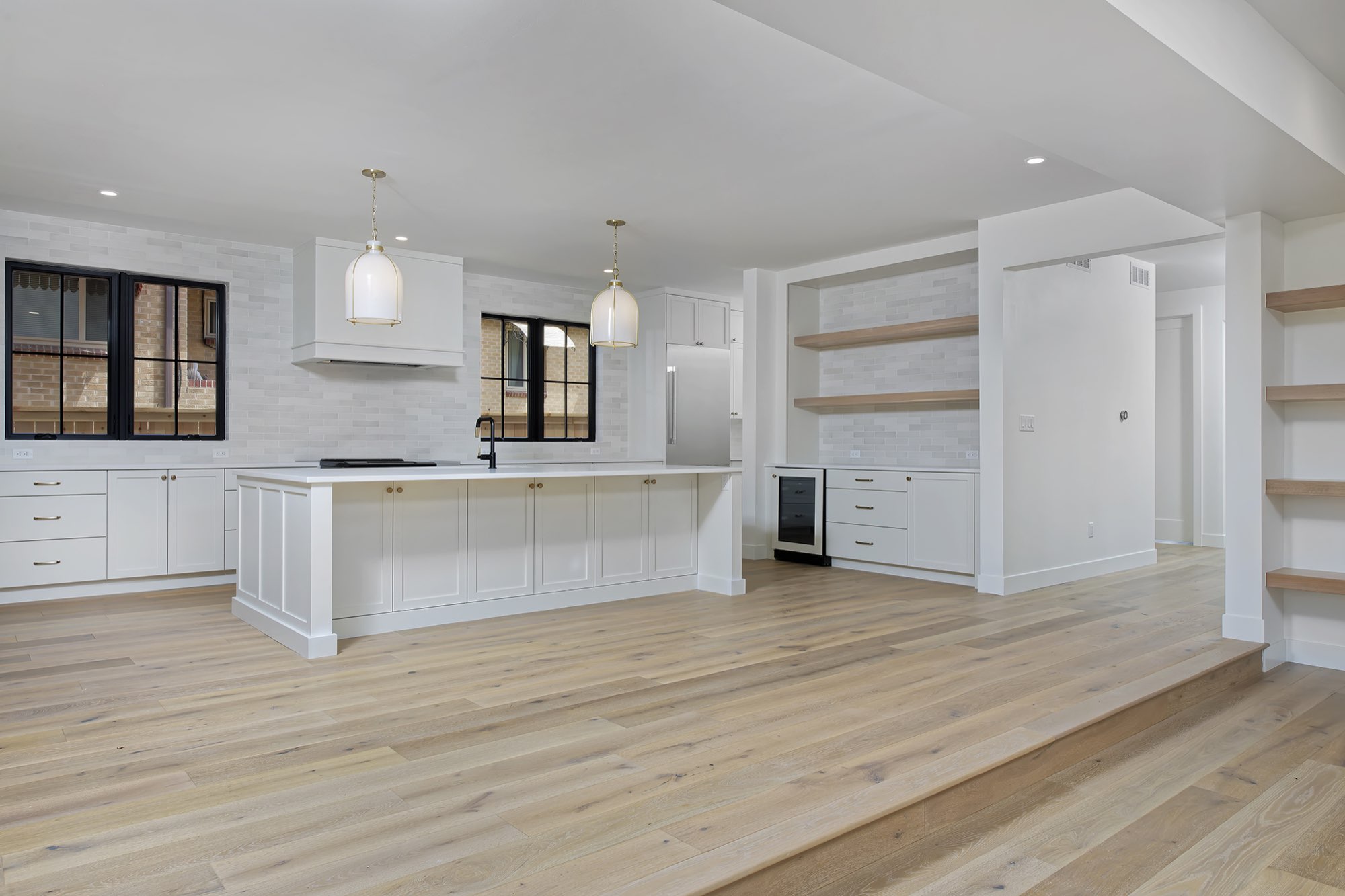 Wide view of the kitchen with a long white island, two pendants, a white hood and shaker cabinets