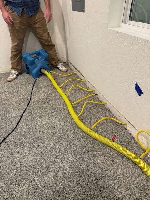Wall cavity drying system pushing air into the wall behind removed baseboards