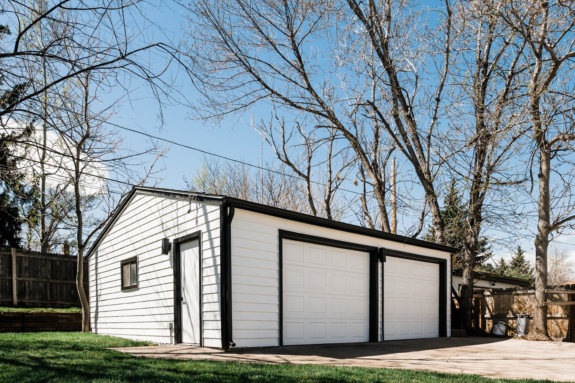 Detached garage with white siding, black trim and two white garage doors