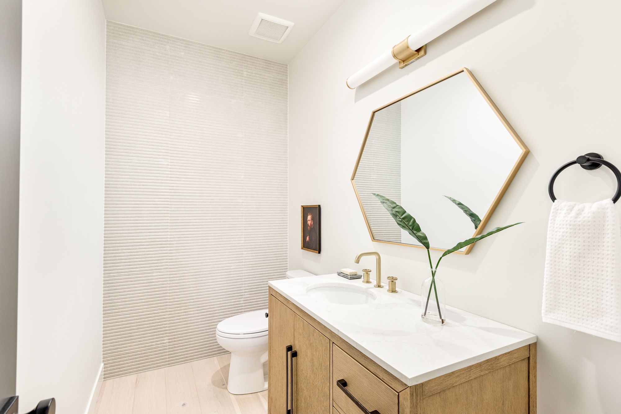 Powder room with a hexagon brass mirror and an oak vanity