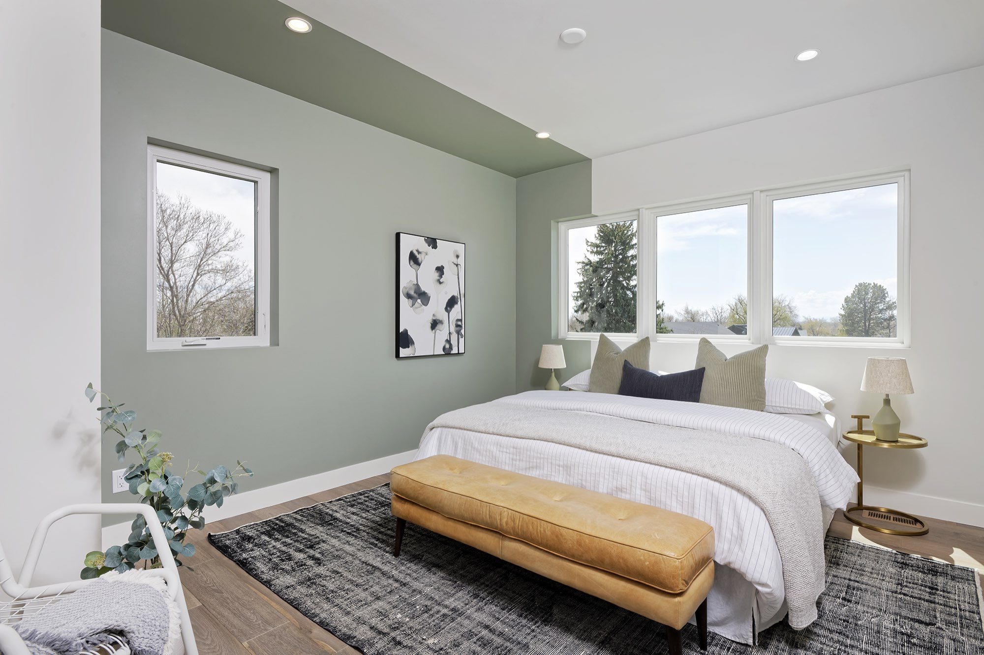 Primary bedroom with a sage green accent wall and ceiling edge, a window group and wood floors