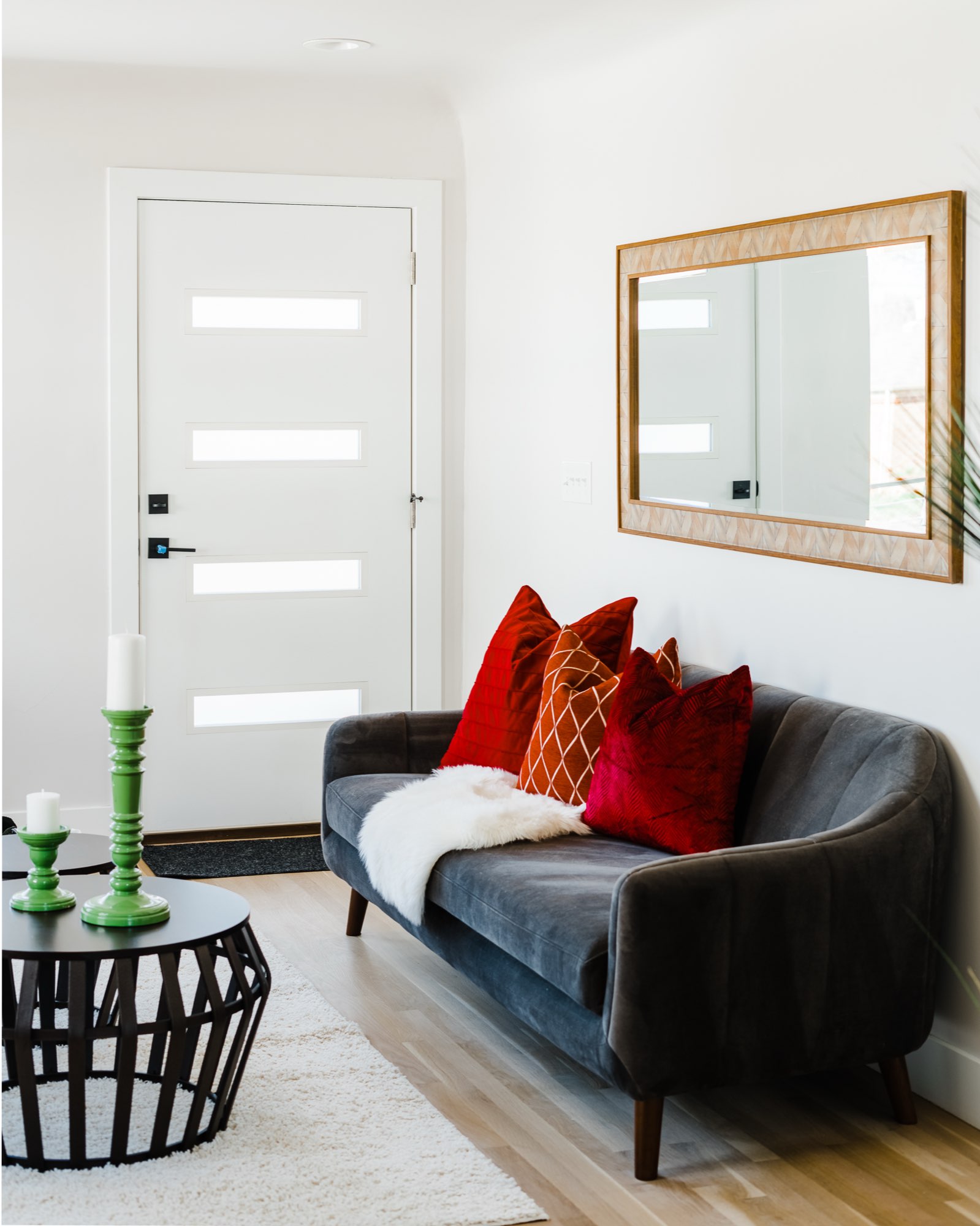 Gray sofa with red and orange pillows, a framed mirror and a white interior door with four narrow windows