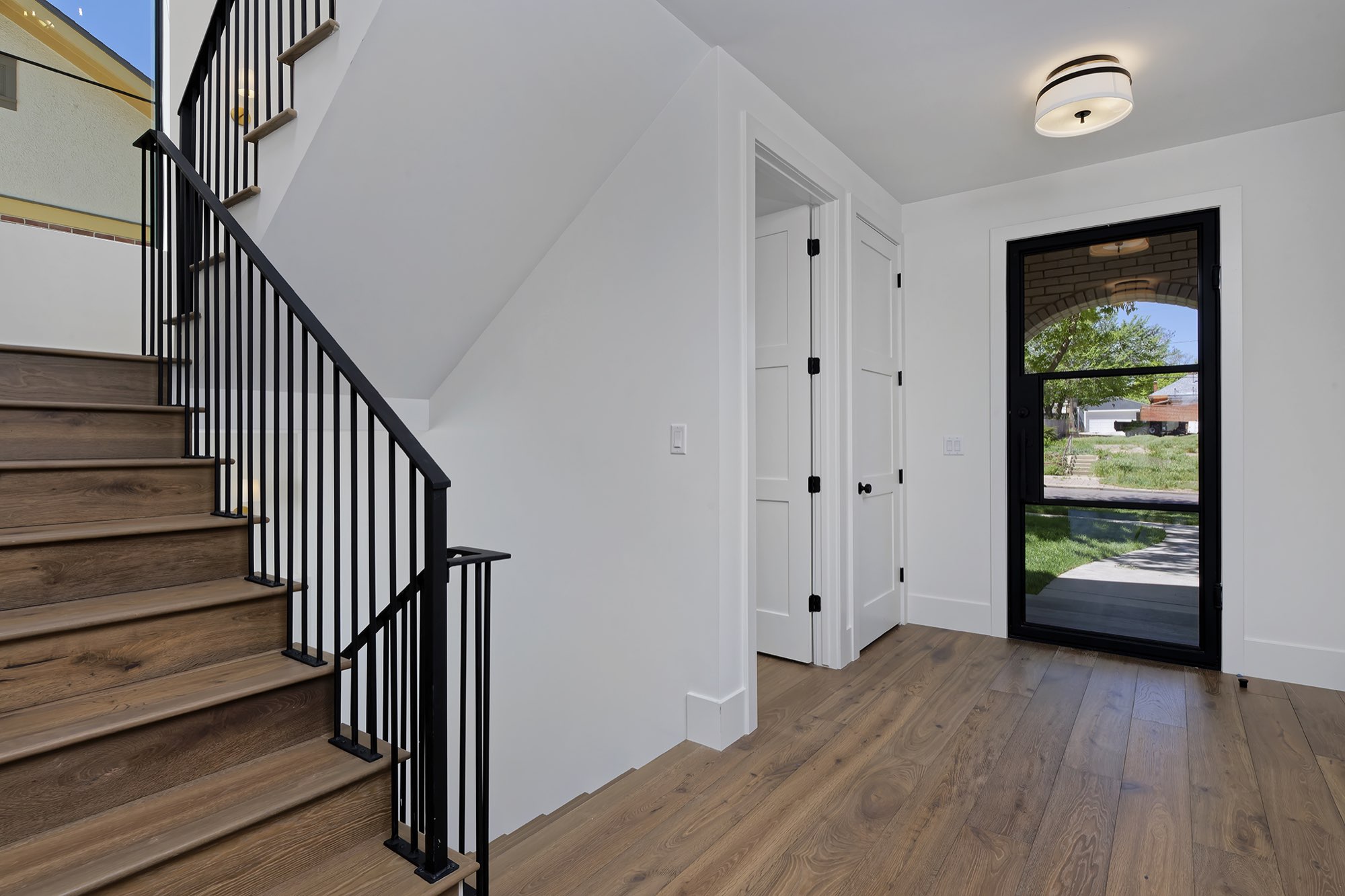 Entry with wood stair treads, black iron railing and a glass front door with an arched view of the porch