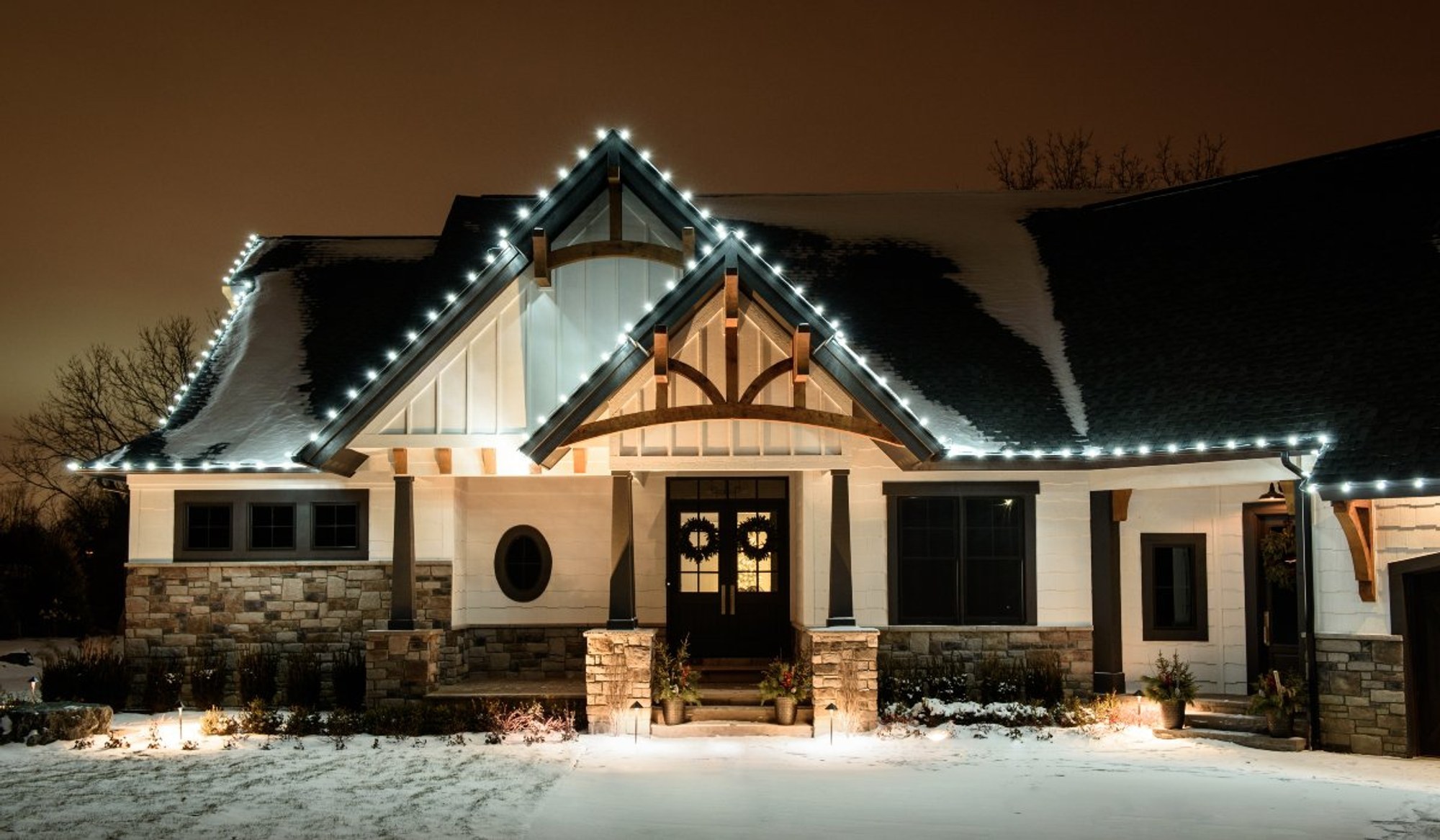 Home with warm white roofline lights and lit mini trees