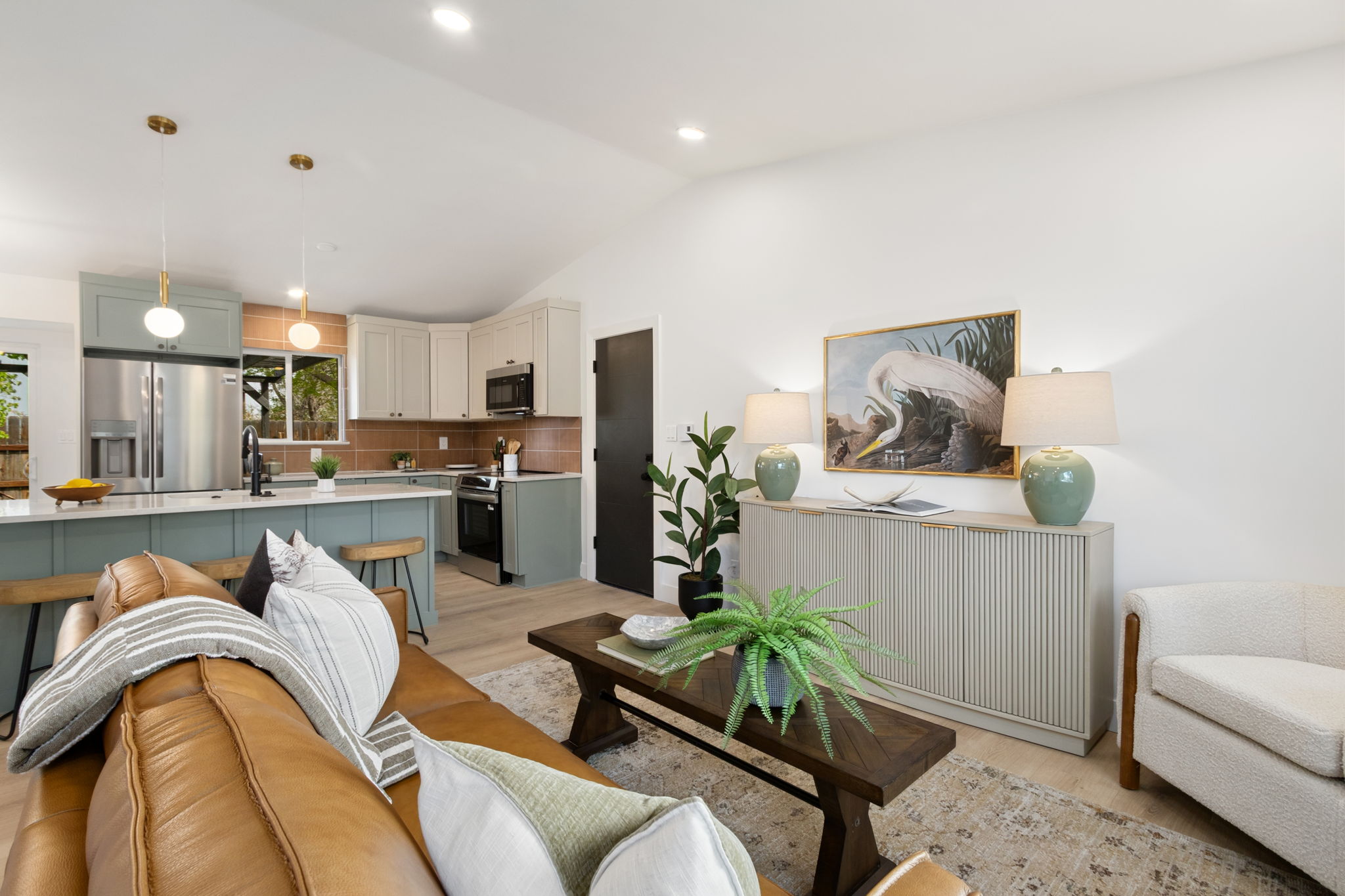 Living room on the open main level looking toward the kitchen, with light plank flooring and a vaulted ceiling