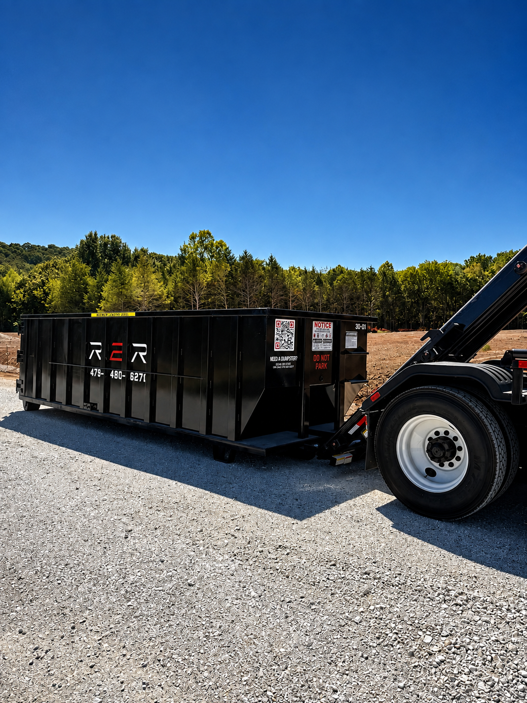 R2R roll-off dumpster rolling off the back of the truck onto a gravel pad