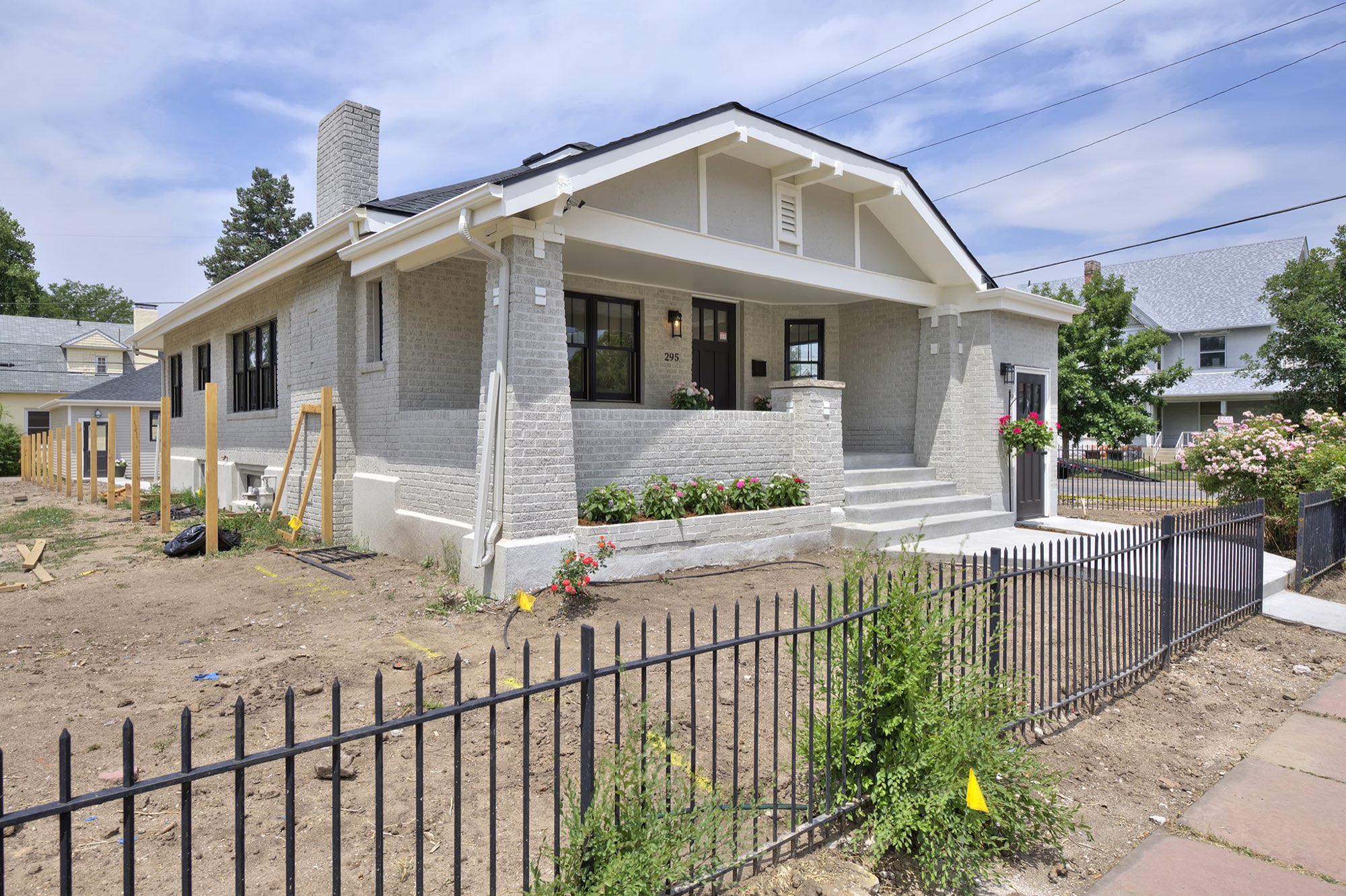 Corner view of the renovated Denver bungalow with its gabled porch roof, pale gray brick and black iron fence