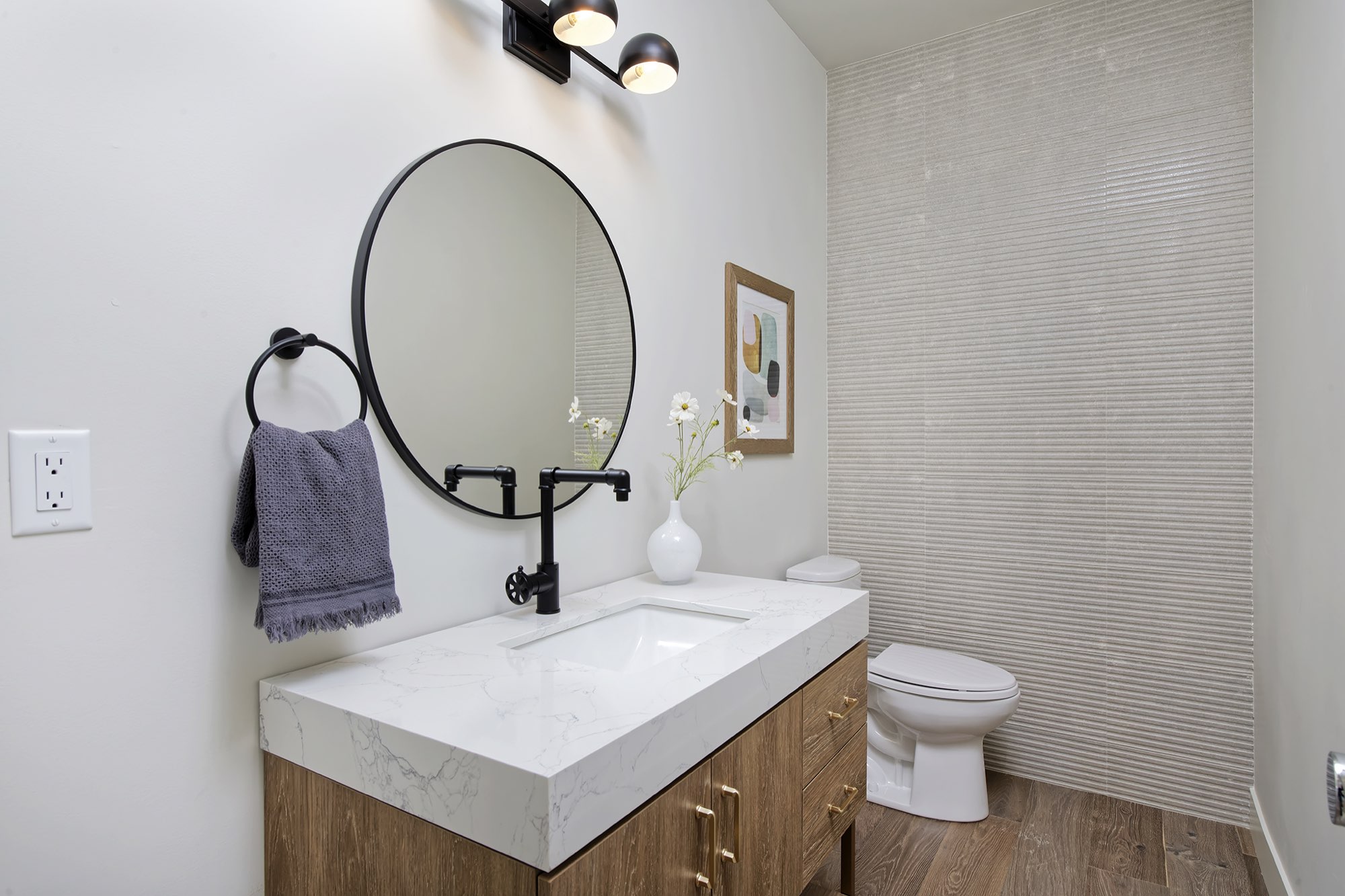 Powder room with a wood vanity, round black mirror, black industrial faucet and a ribbed tile wall
