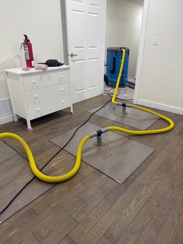 Hardwood floor drying system with drying mats and an extraction unit running in a bedroom
