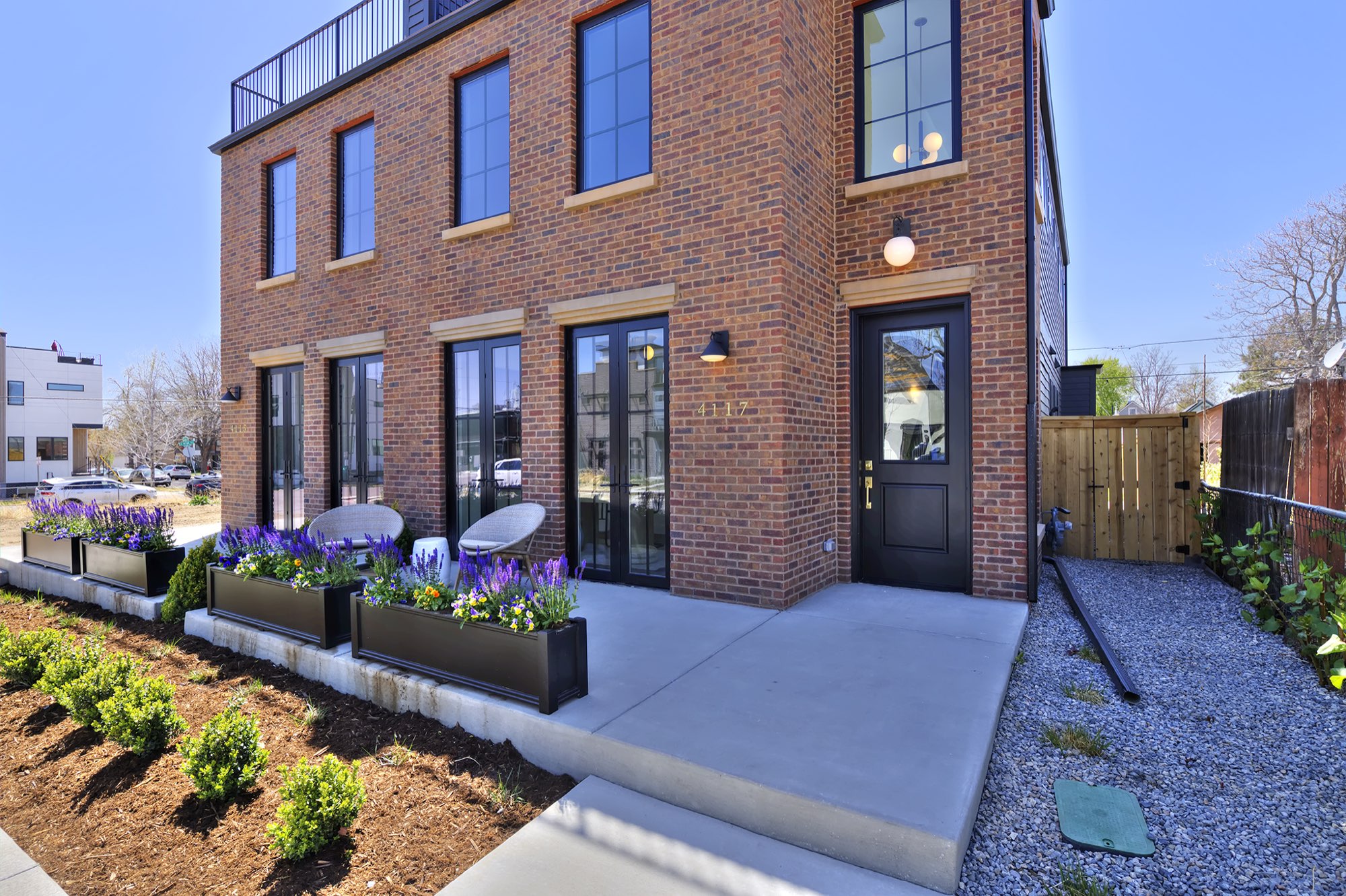 Corner view of the red brick front with tall black-framed windows, globe lights, planter boxes and a concrete walk