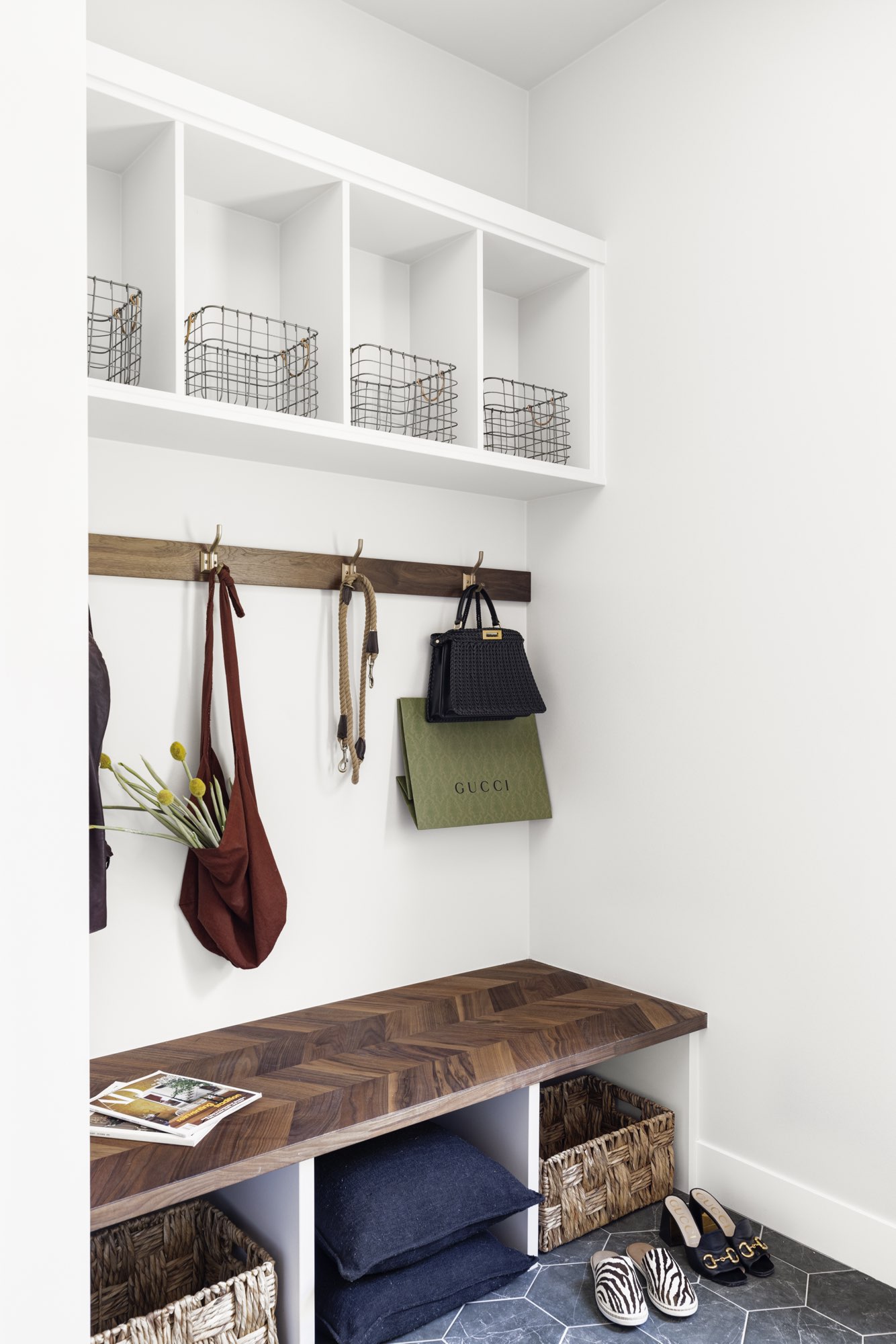Mudroom with a built-in bench with a herringbone wood seat, cubbies, hooks, open shelves and a dark hex tile floor