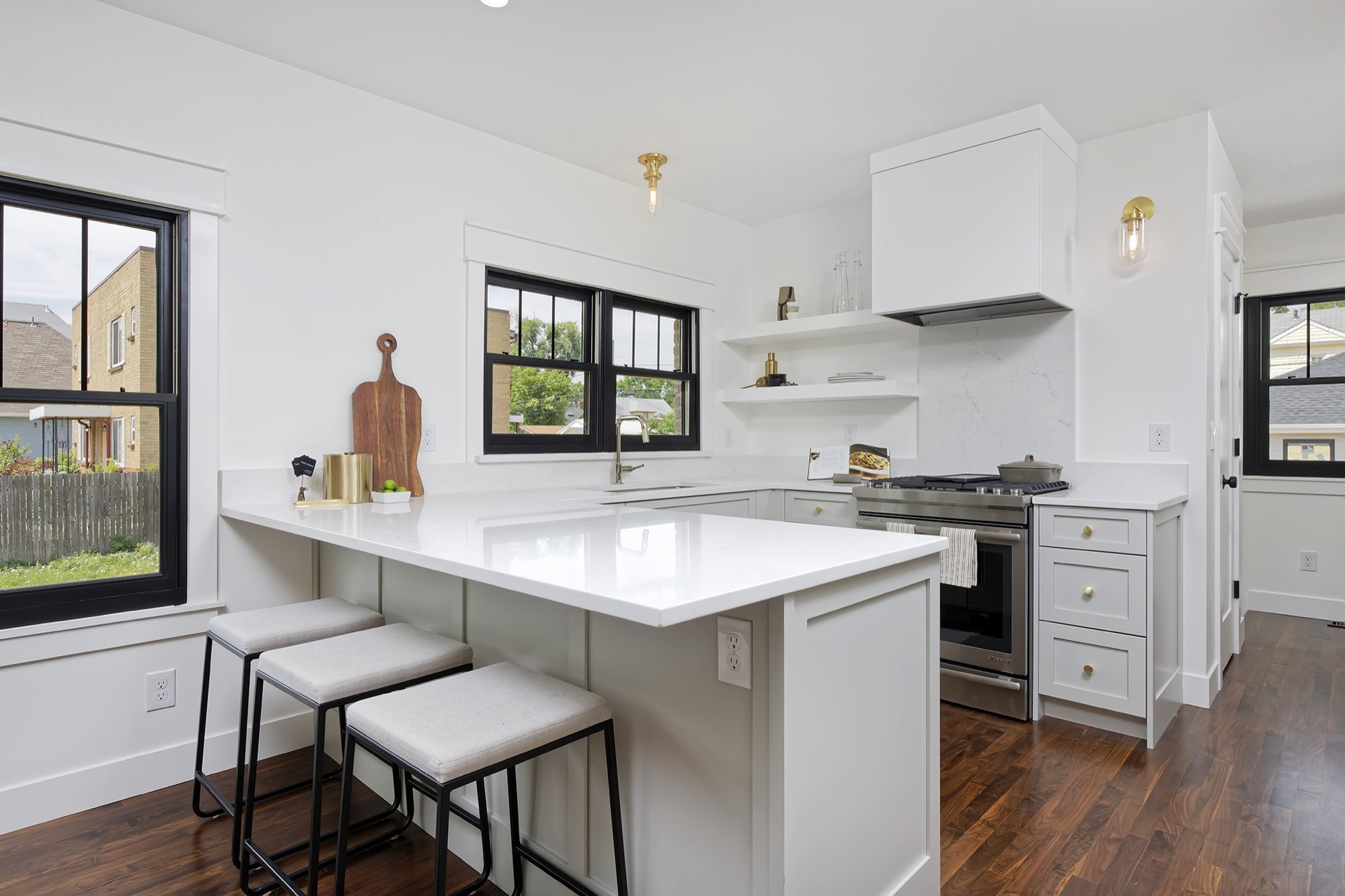 Kitchen peninsula with three counter stools, a white hood and floating white shelves