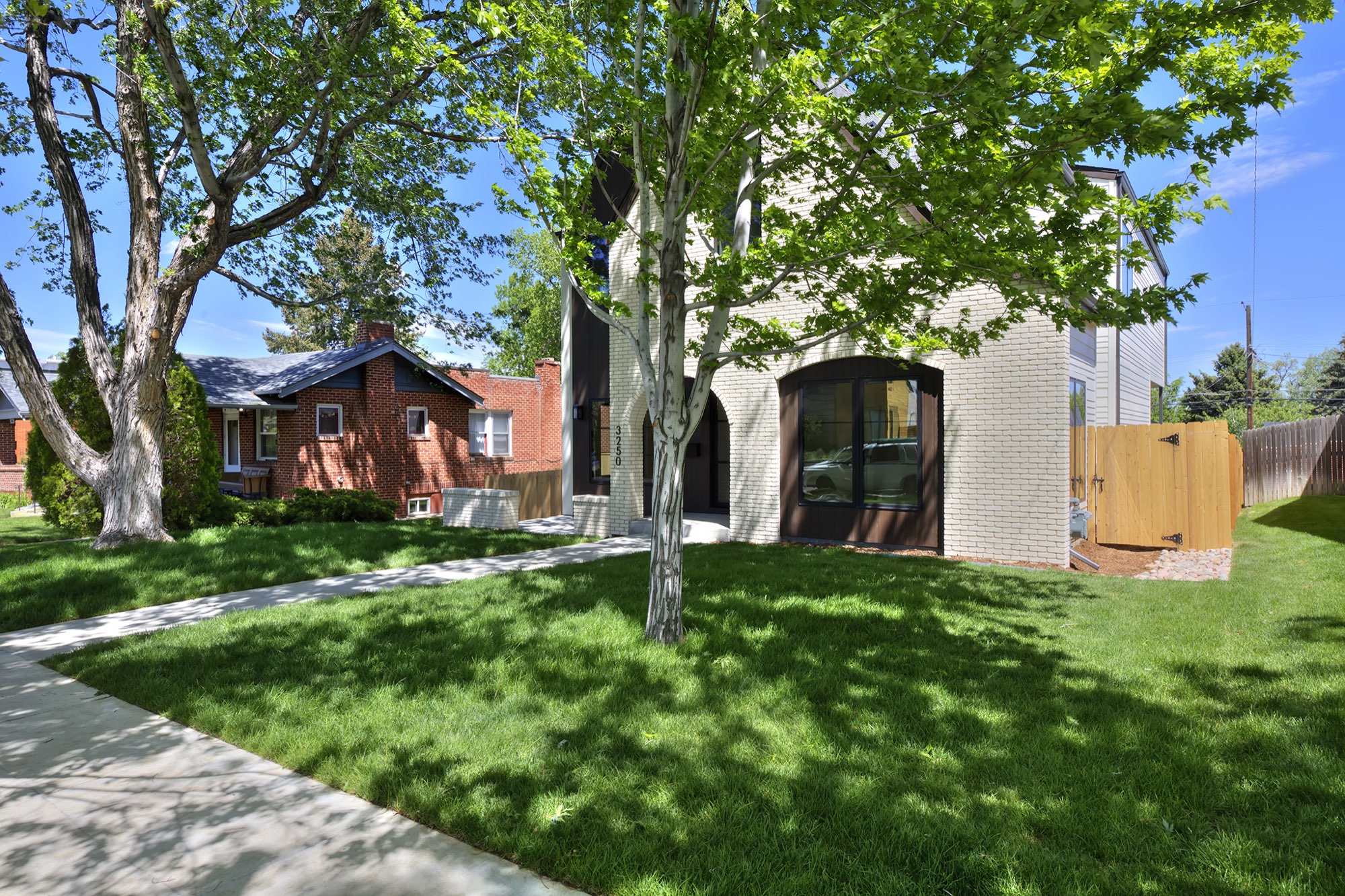 White brick gable of the new home seen through mature trees across the front lawn and walk