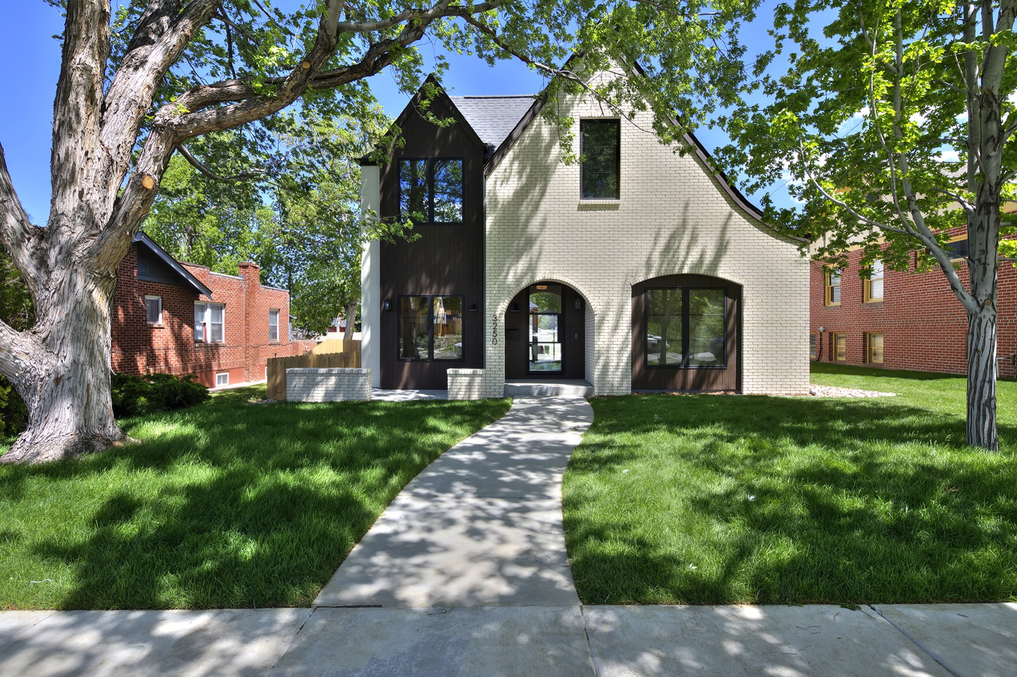 Front of the new Tudor-style custom home in Denver with a white brick gable, dark vertical siding, arched entry and a front lawn