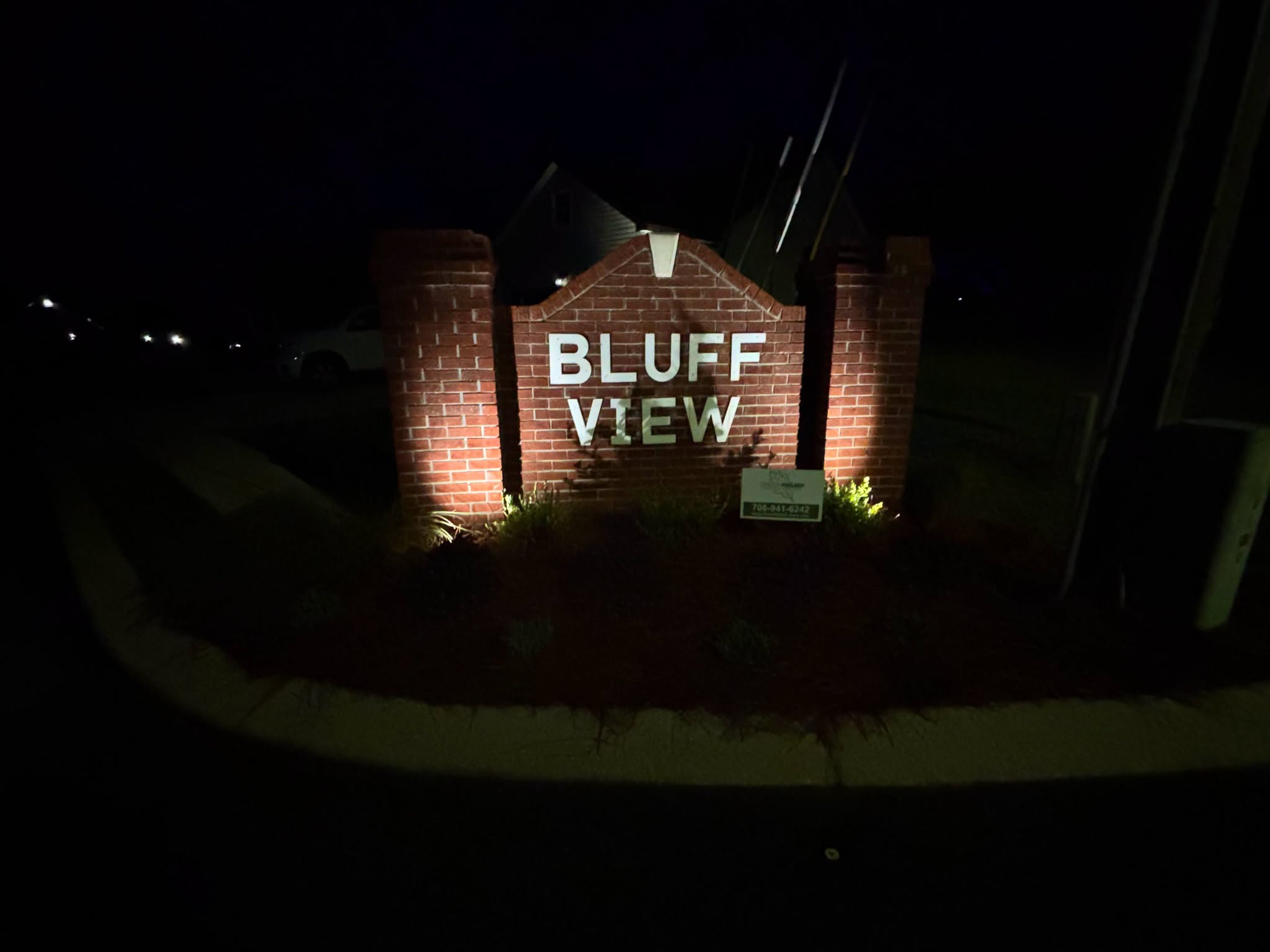 Neighborhood entrance sign lit at night with landscape lighting