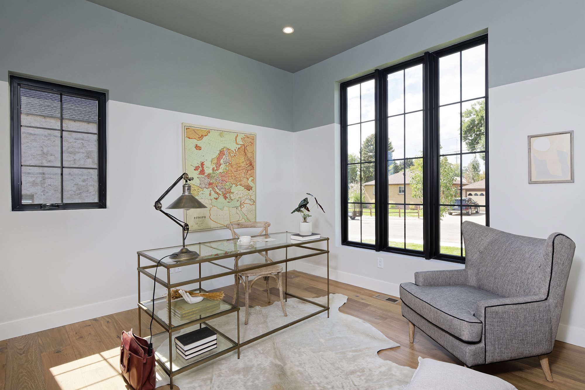 Office with a sage green ceiling, white walls, three tall black-framed windows and wood floors