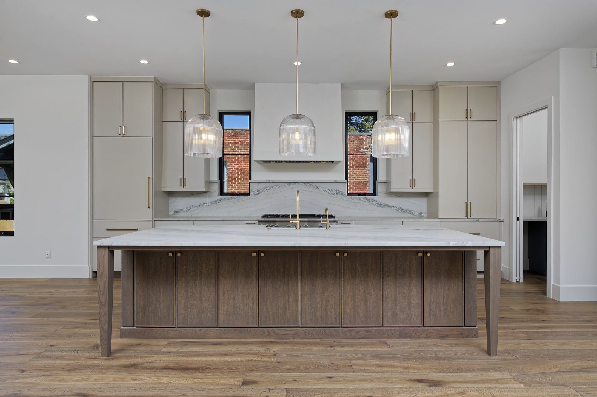 Long kitchen island with a wood-tone base and white stone top, three ribbed glass pendants and cream cabinets behind