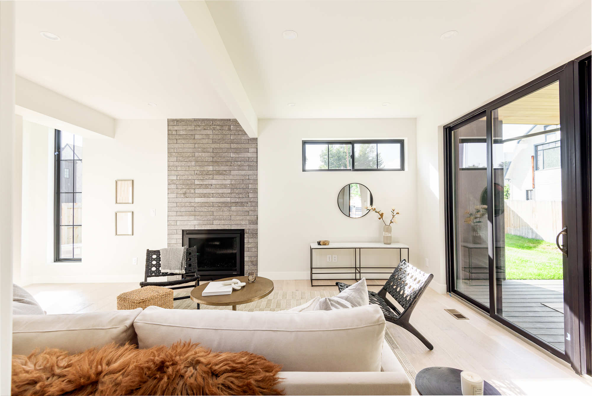 Living room with a gray stacked fireplace wall, a black slider to the deck and a high black-framed window