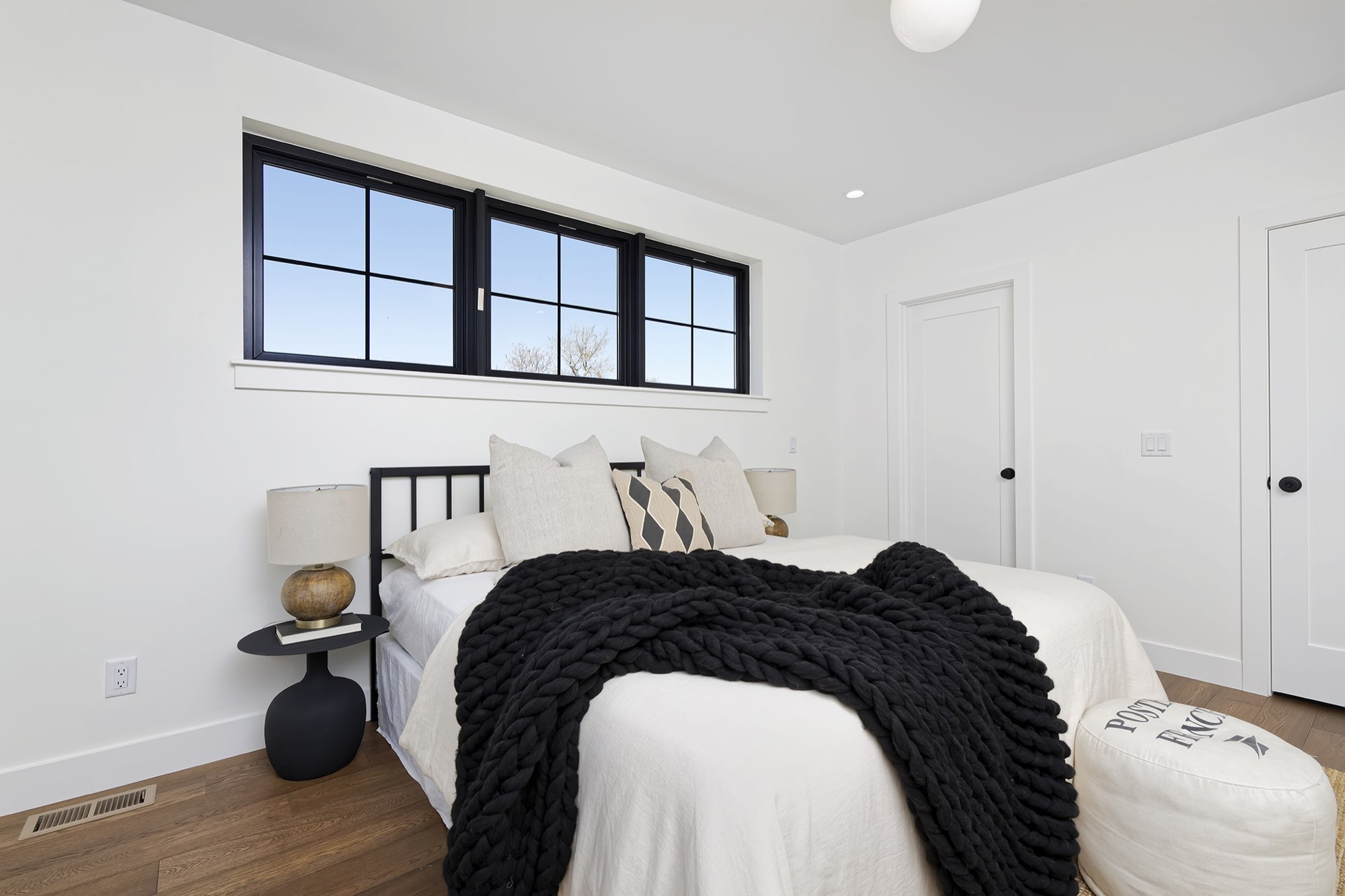 Bedroom with a wide row of black-framed windows above the bed and wood floors