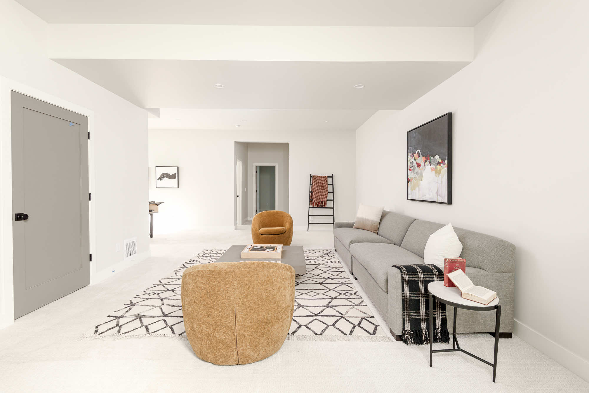 Lower-level family room with a gray sofa, rust swivel chairs, a patterned rug and a game table