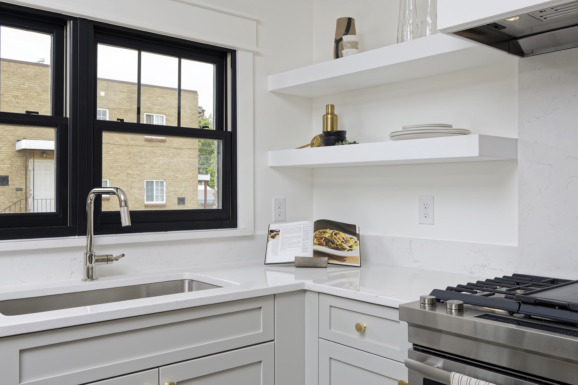 Kitchen corner with a stainless sink under black-framed windows and floating white shelves