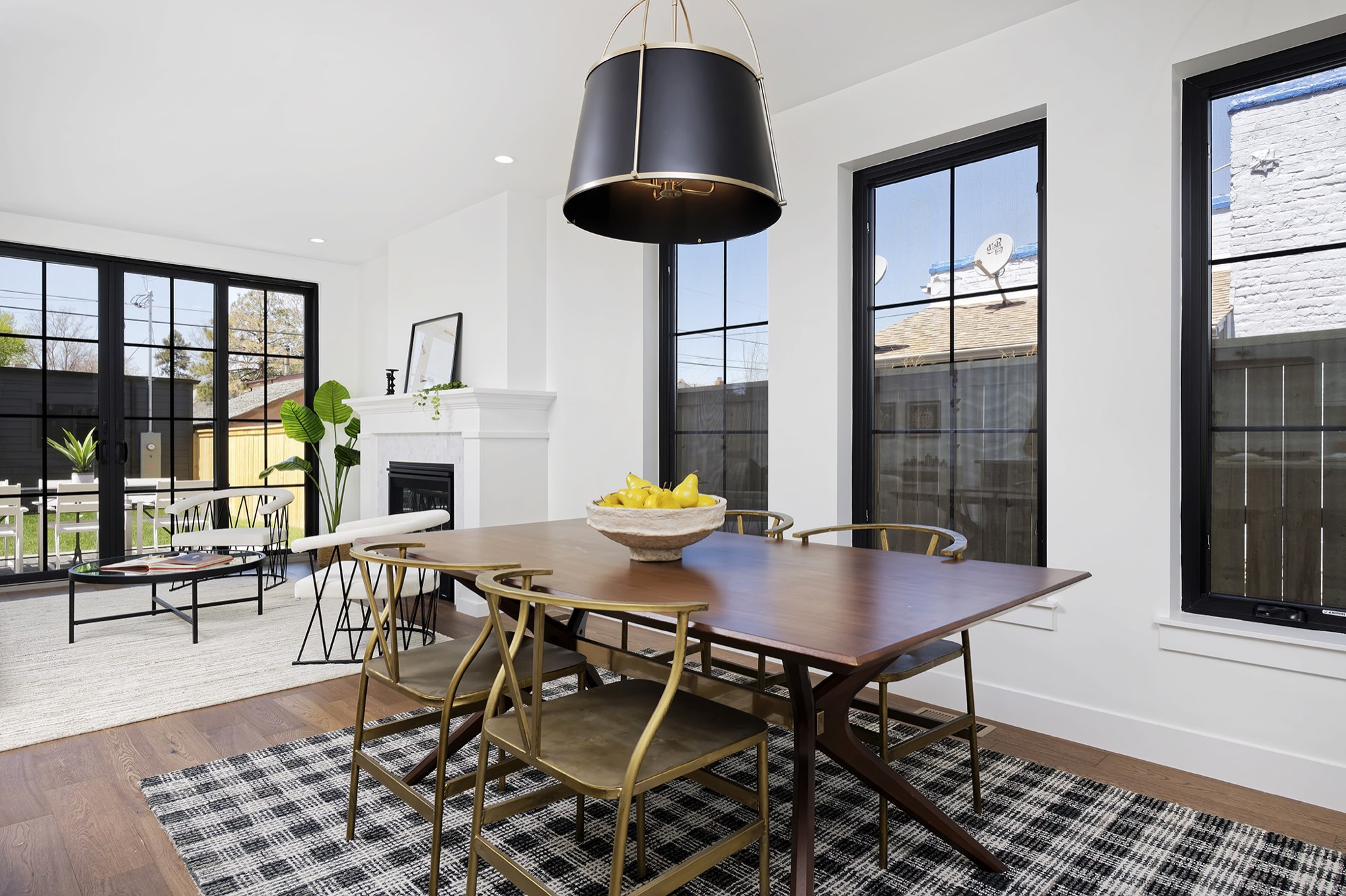 Dining table under a black drum pendant with tall black-framed windows and wood floors