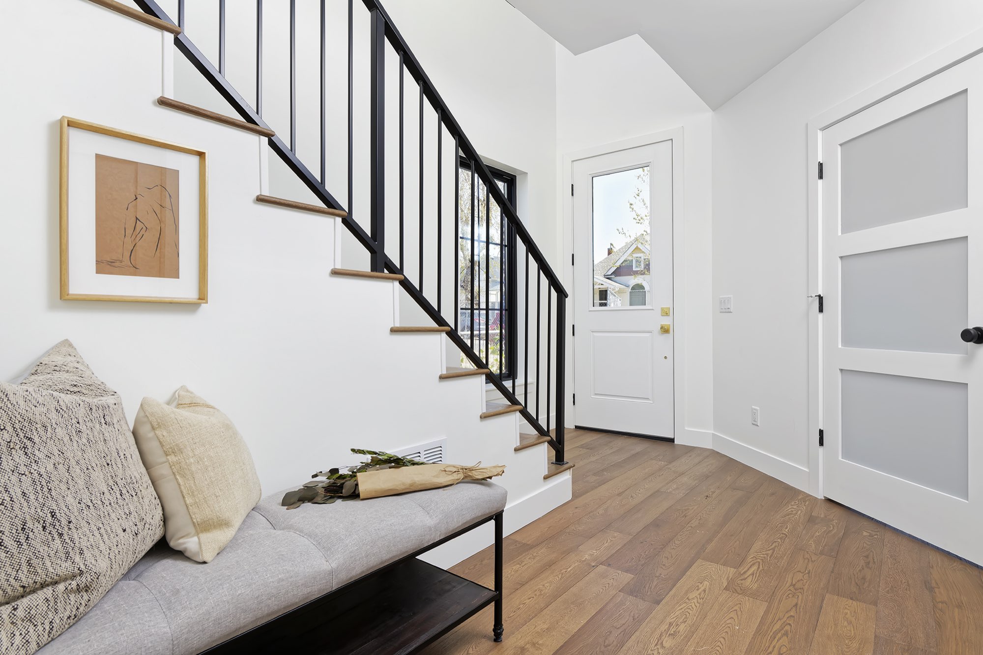 Entry with a stair, black metal railing, wood floors, a door with frosted glass panels and a bench