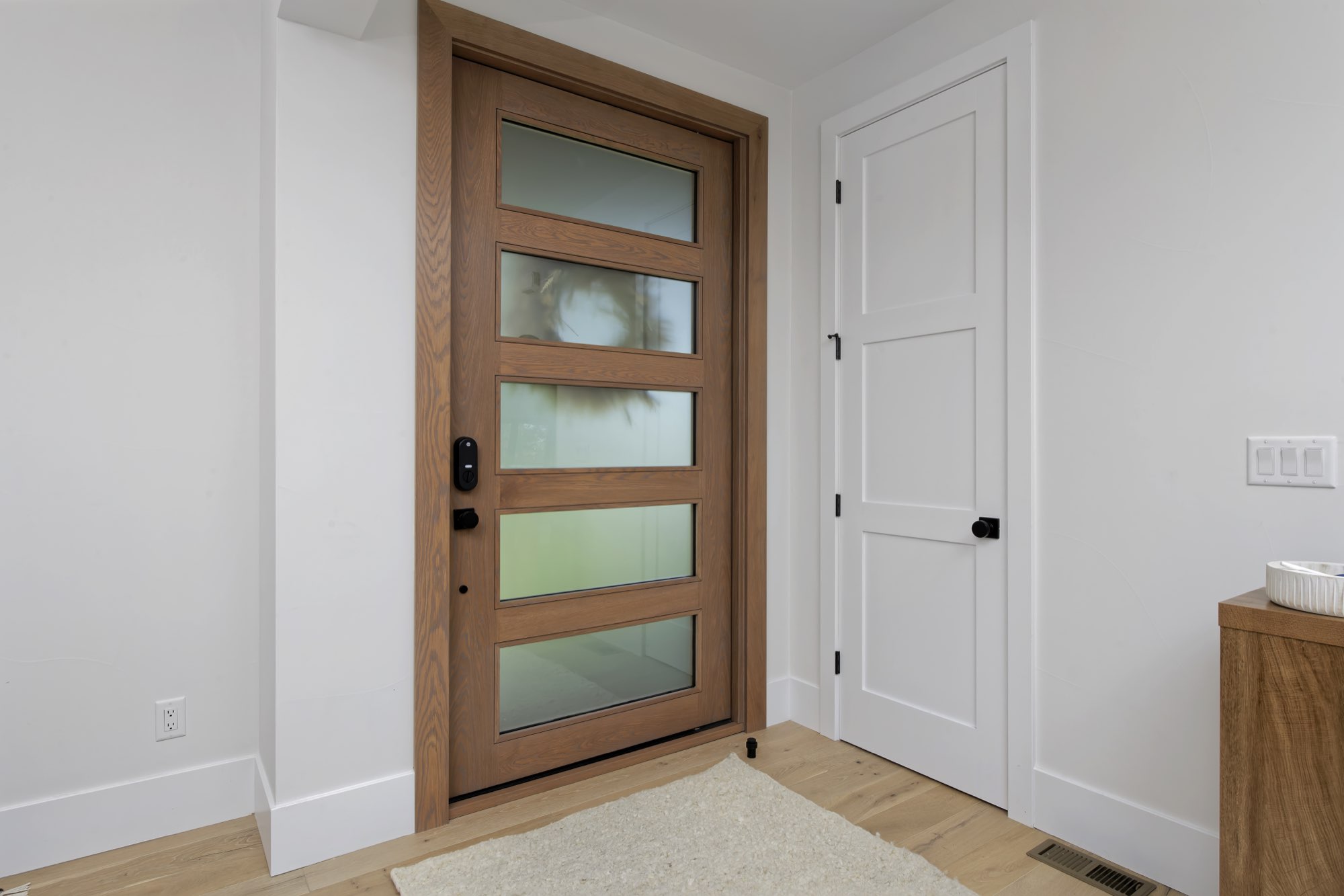 Entry with a wood front door of frosted glass panels, a paneled white door and wood floors