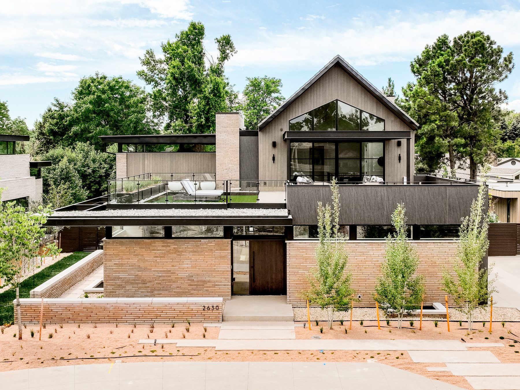 Modern custom home with long brick walls, a wood-clad gable with tall black windows and a rooftop terrace