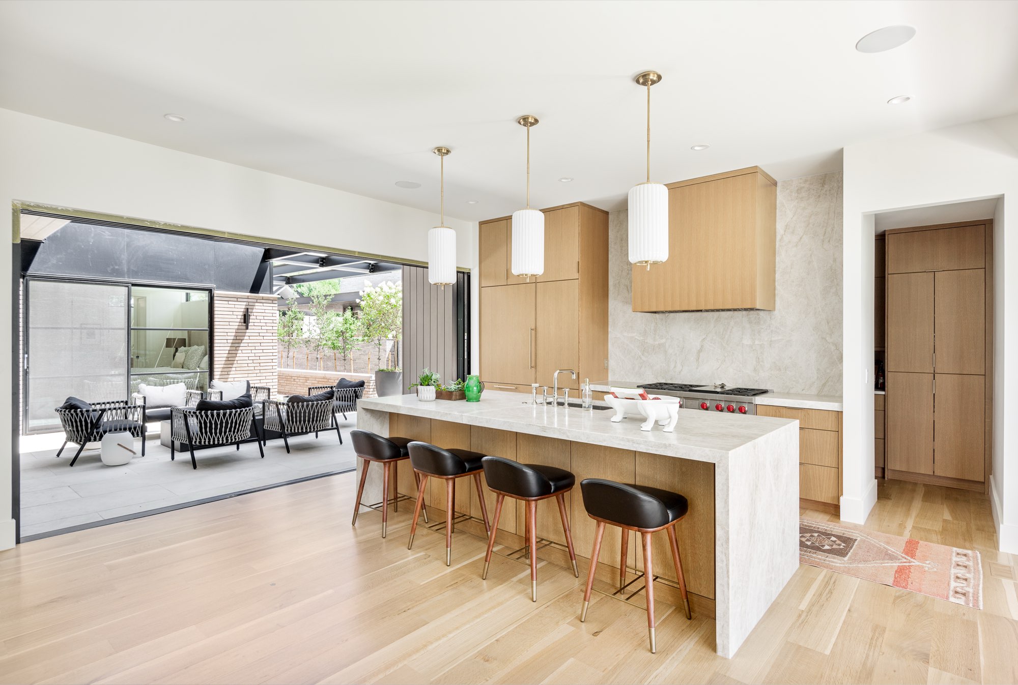 Kitchen island with four black leather stools and white fluted pendants, with glass doors open to the patio