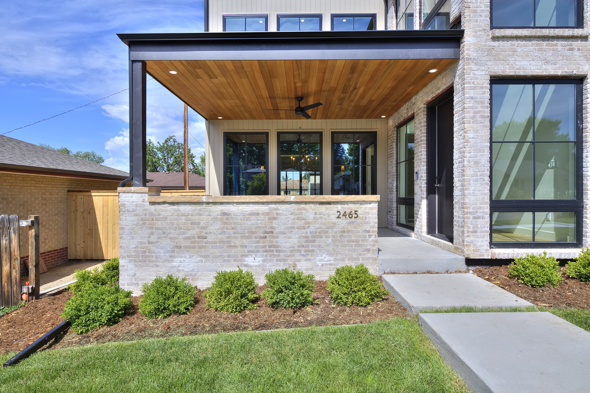 Covered front porch with a wood-plank ceiling, ceiling fan and low brick wall beside the black front door