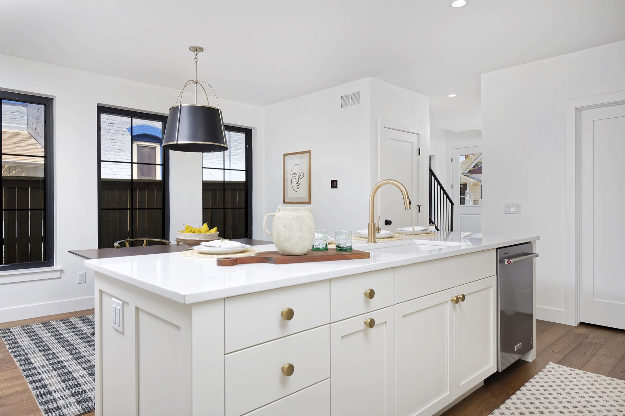 Kitchen island with brass pulls and a brass faucet, a black drum pendant above and black-framed windows beyond