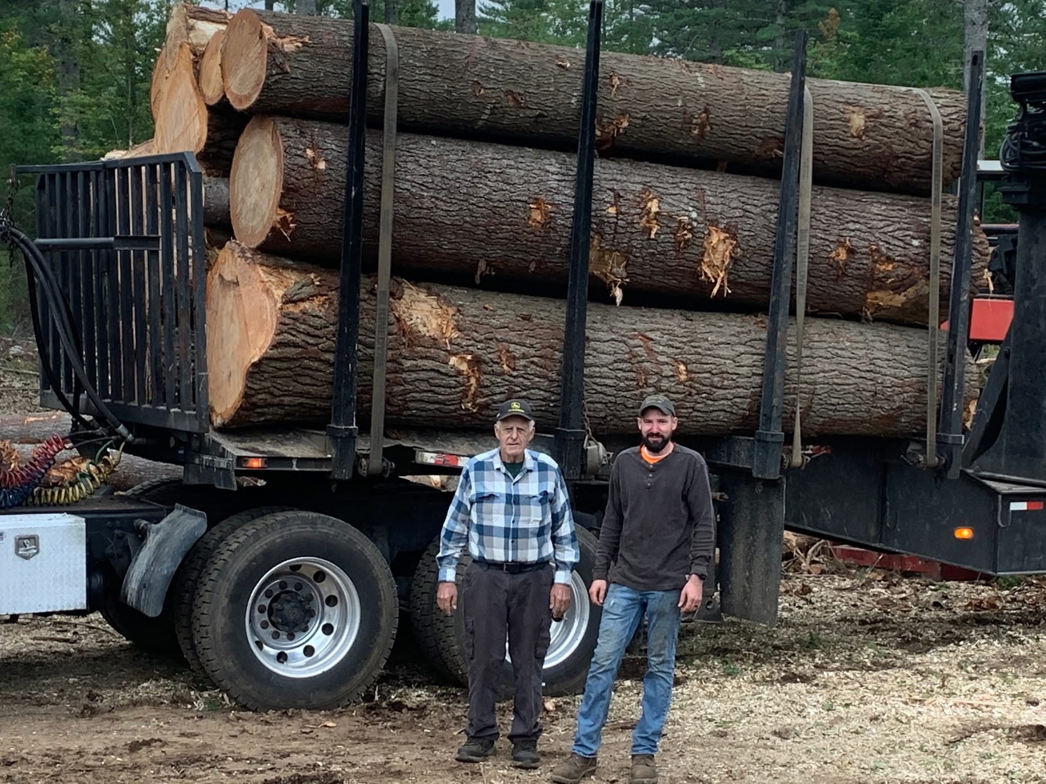 Trevor Chaplin standing with family beside a fully loaded log truck at a landing in Sebago, Maine.