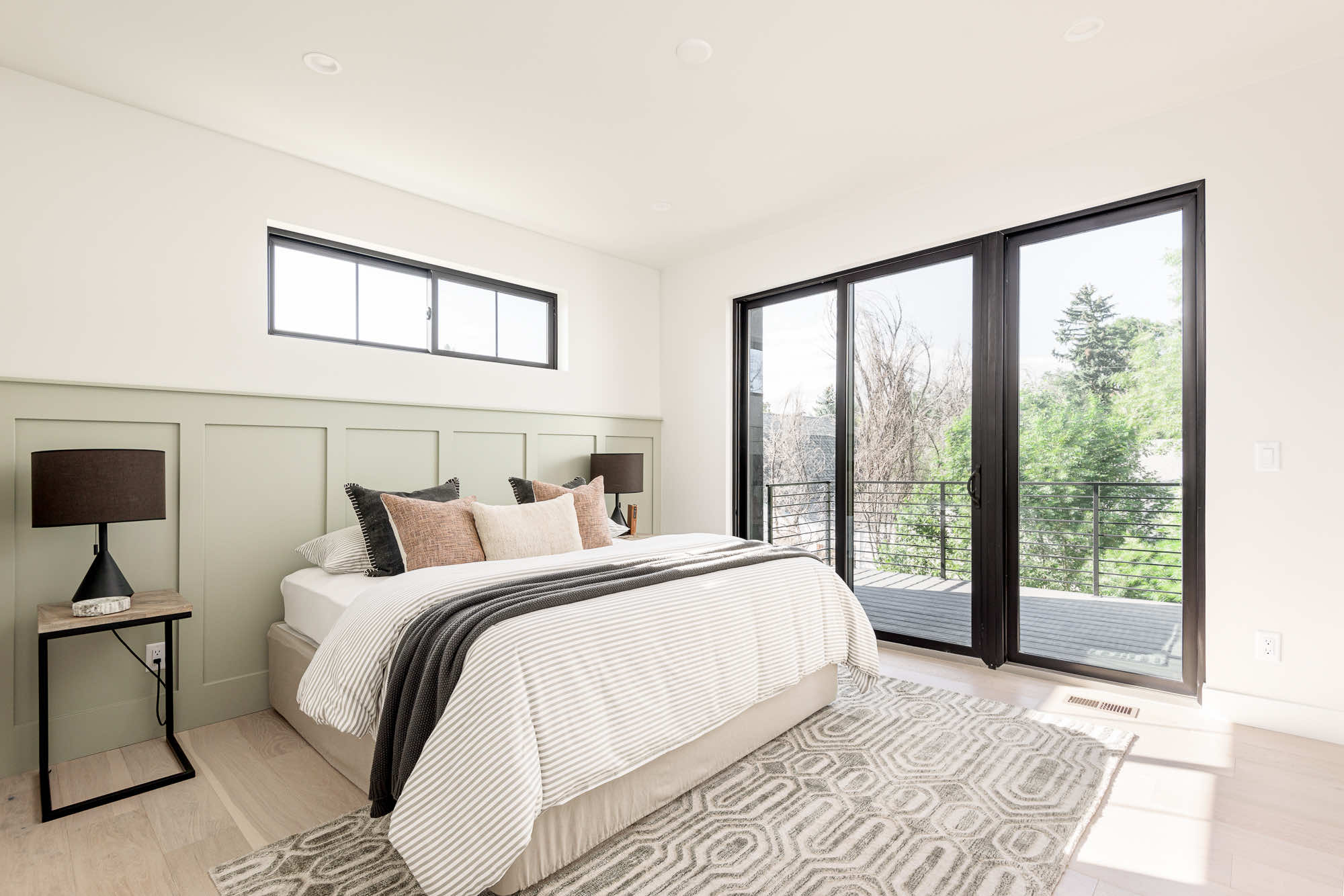 Primary bedroom with a green paneled wall, striped bedding and a black slider to the balcony