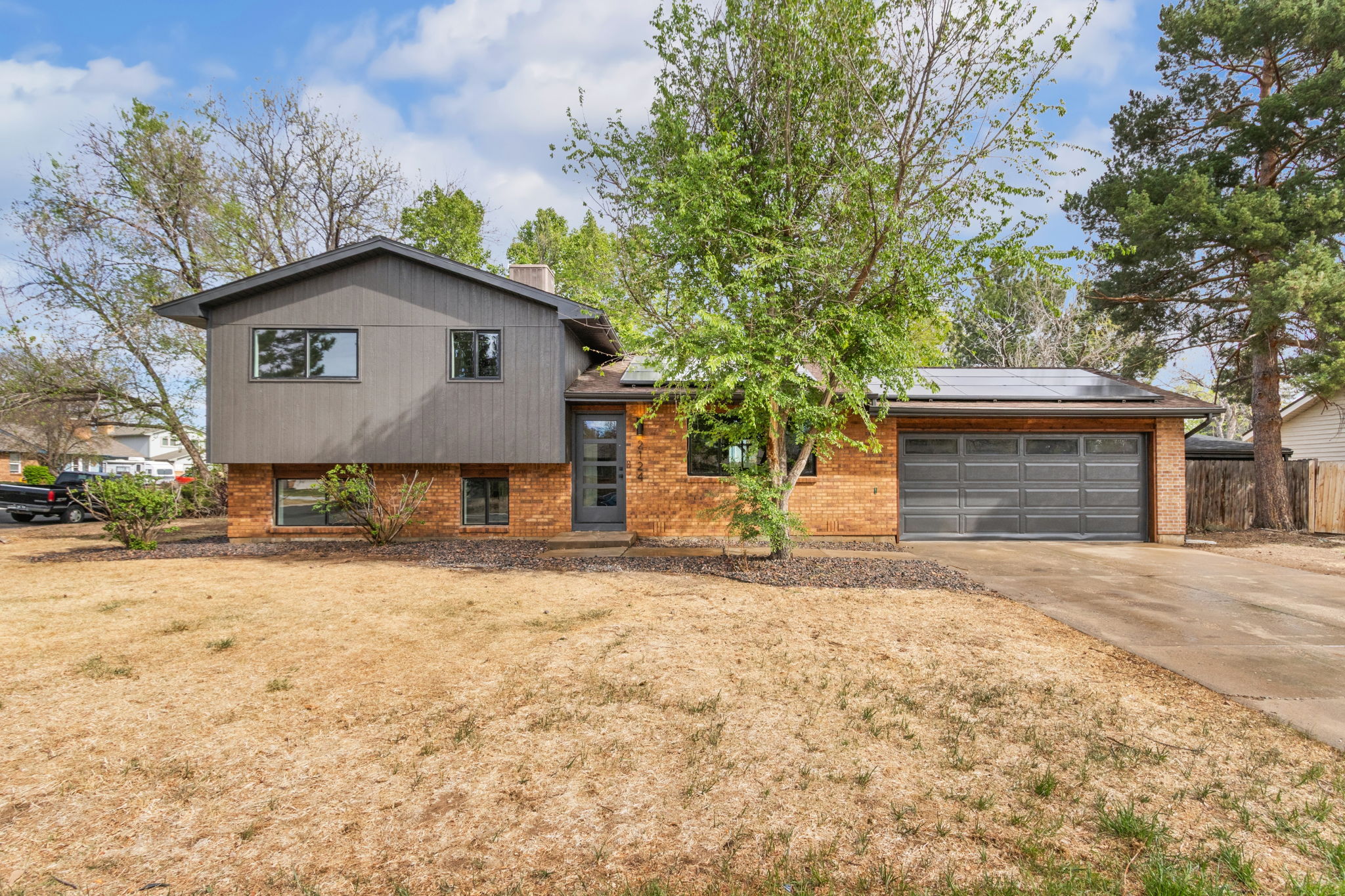 Front of the remodeled brick split-level in Fort Collins with vertical gray siding on the upper level, black-framed windows and the garage on the right