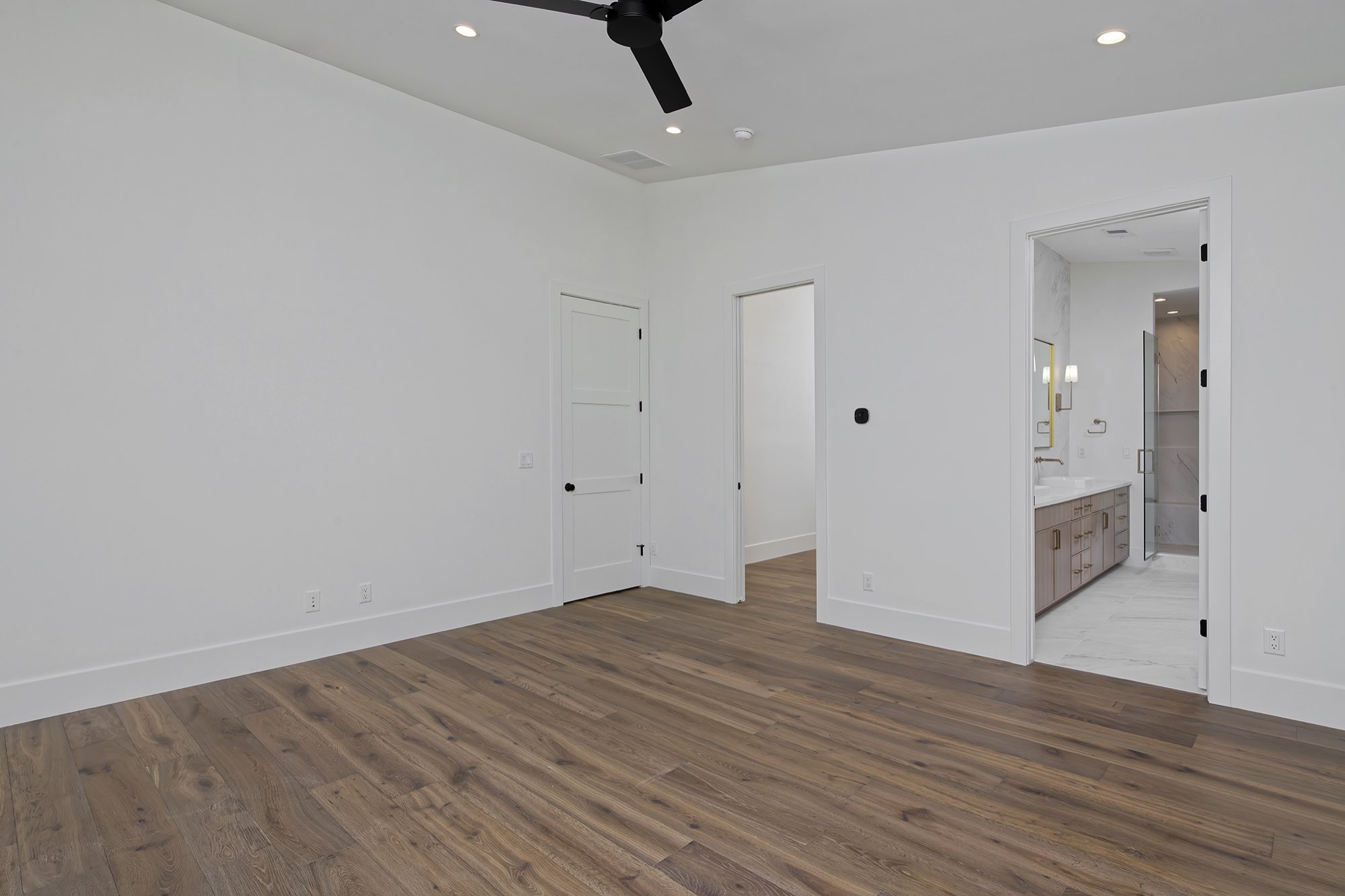 Primary bedroom with wood floors, a ceiling fan and a doorway to the bath