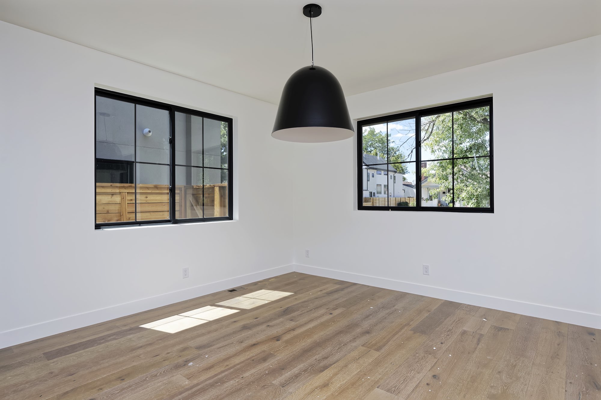 Dining area with a black dome pendant, two black-framed windows and light wood floors