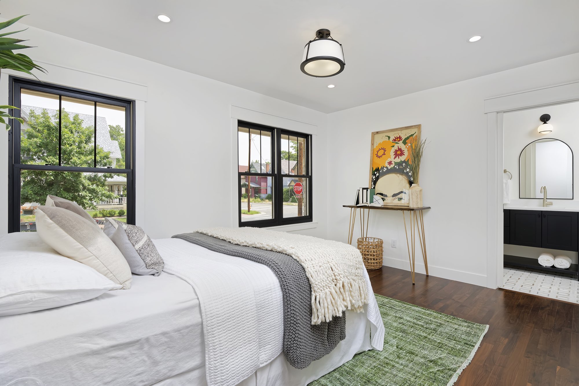 Bedroom with dark wood floors, black-framed windows on two walls and a doorway to a bathroom