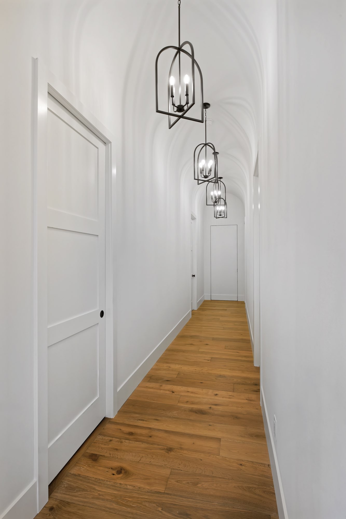 Narrow hallway with a curved white ceiling, black lantern pendants and wood floors
