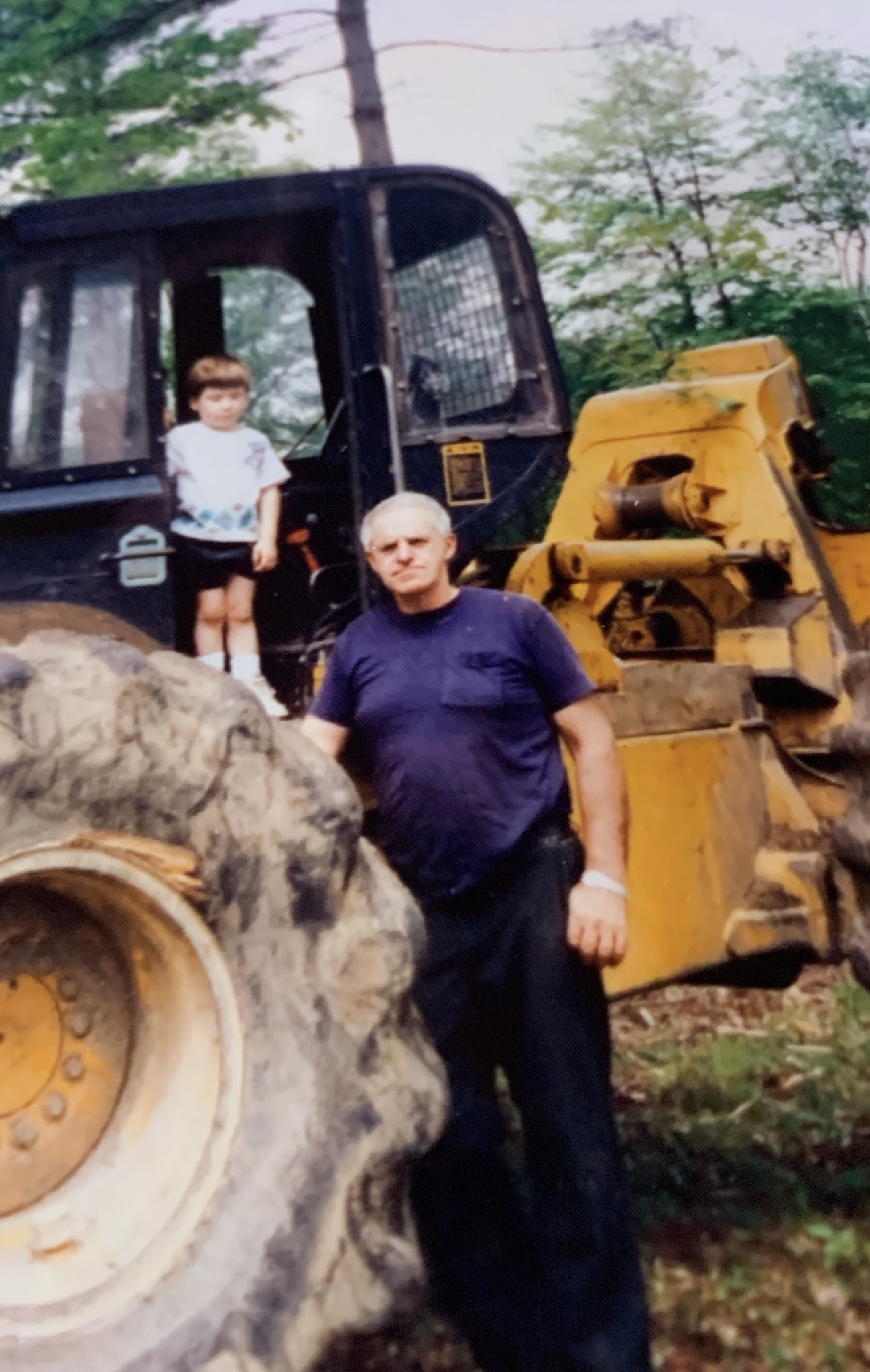 An old family photo of a young Trevor Chaplin standing on a skidder in the woods alongside an older family member.