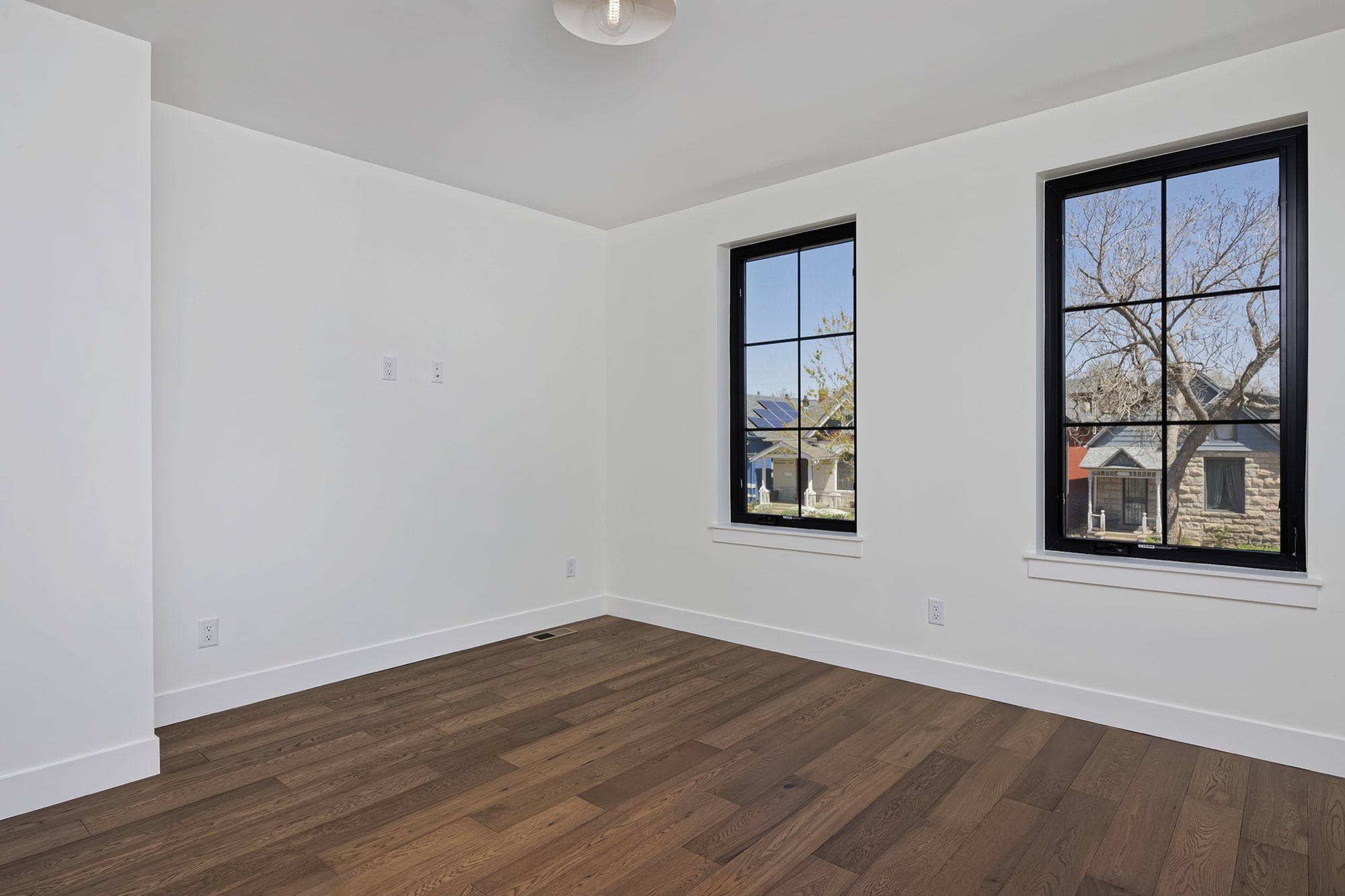 Empty bedroom with two black-framed windows, white walls and wood floors