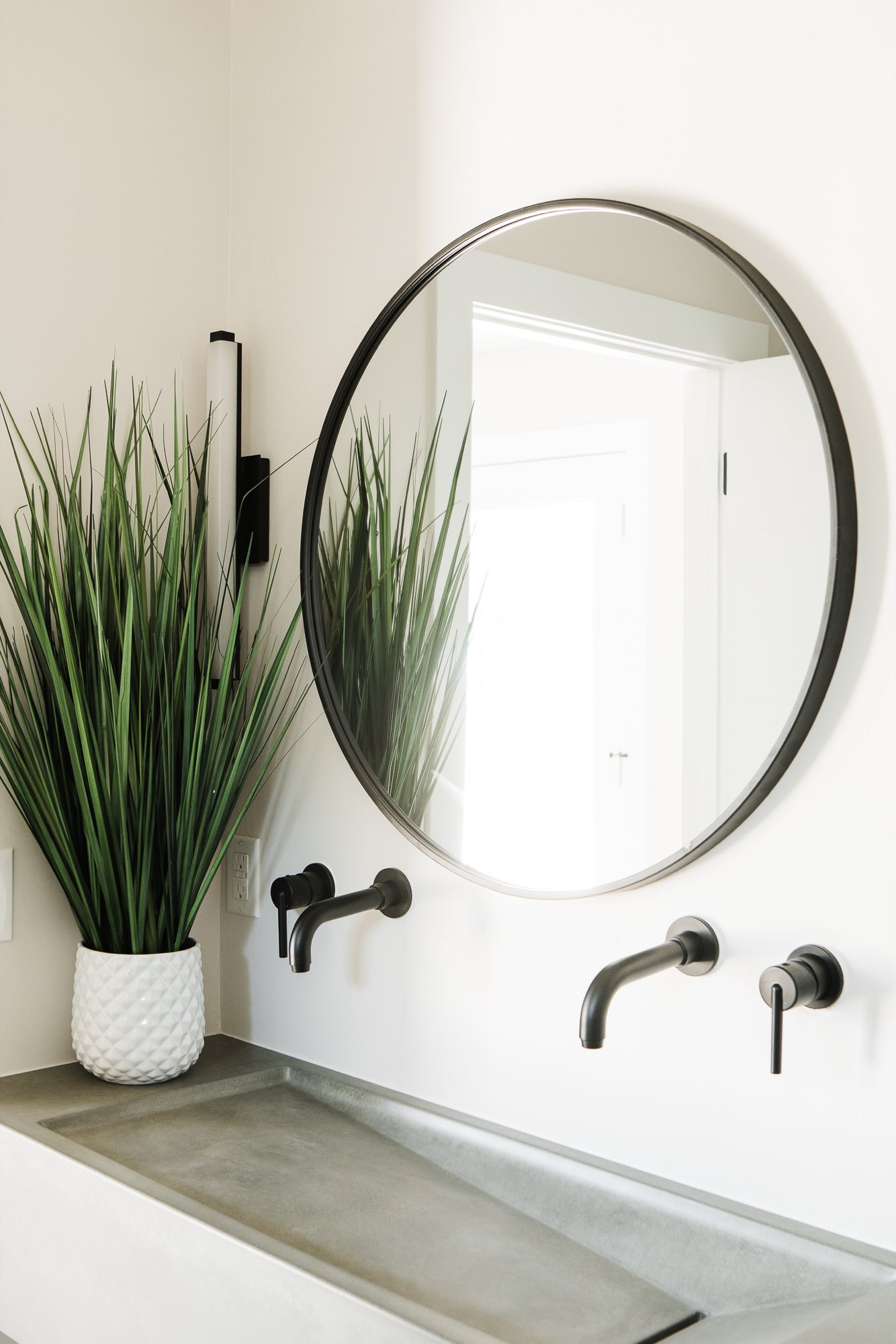 Bathroom with a round black-framed mirror, wall-mounted black faucets and a concrete-look trough sink