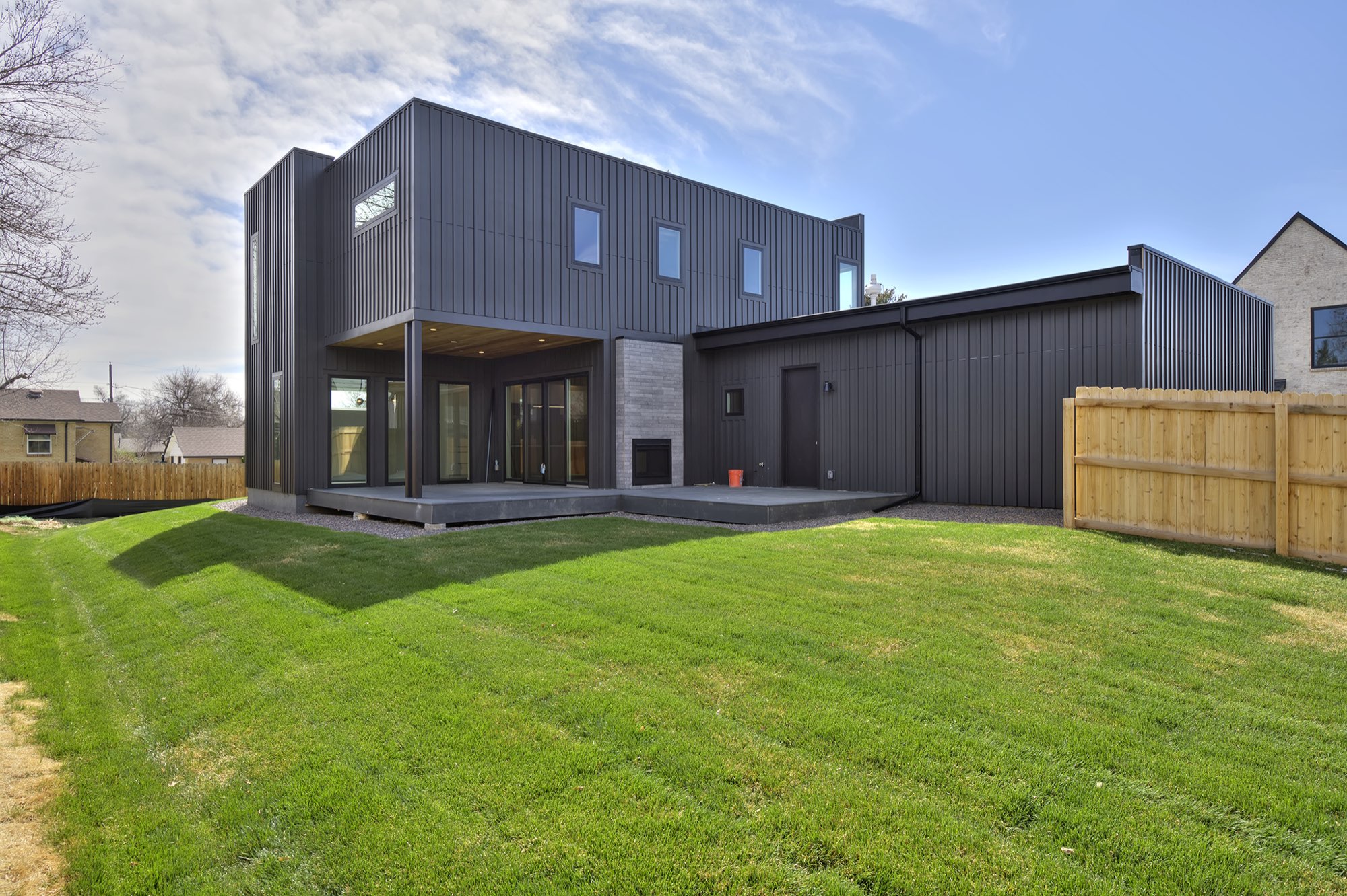 Back of the charcoal home with a covered deck, sliding doors, a gray fireplace wall and a green lawn