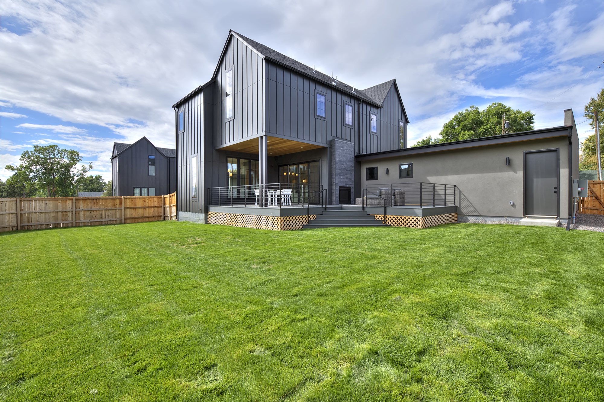 Rear of the house from the lawn, with charcoal siding, a covered deck with a black railing and the garage wing