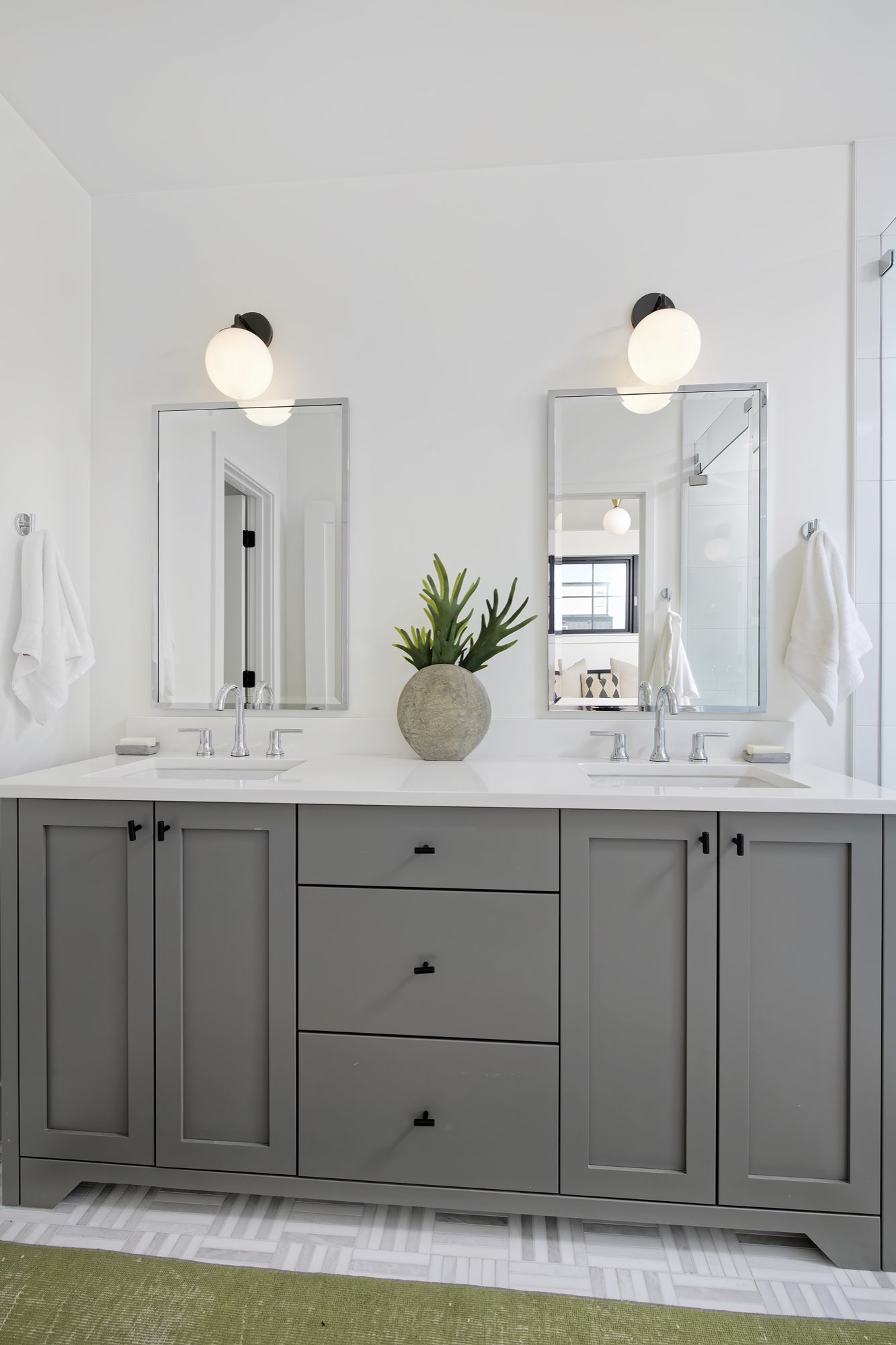 Double vanity with gray cabinets, black pulls, two mirrors and wall sconces over a patterned tile floor