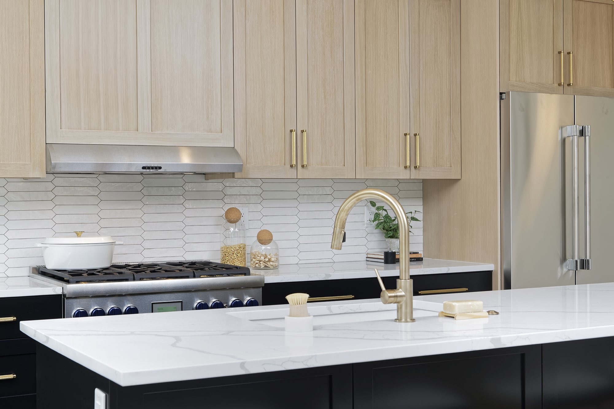 Close view of the white veined countertop, brass faucet and light wood upper cabinets with brass pulls