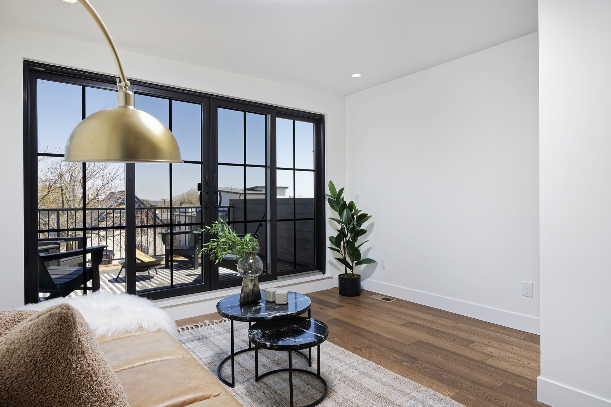 Lounge with wide black-framed glass doors opening to the rooftop deck, wood floors and a brass floor lamp